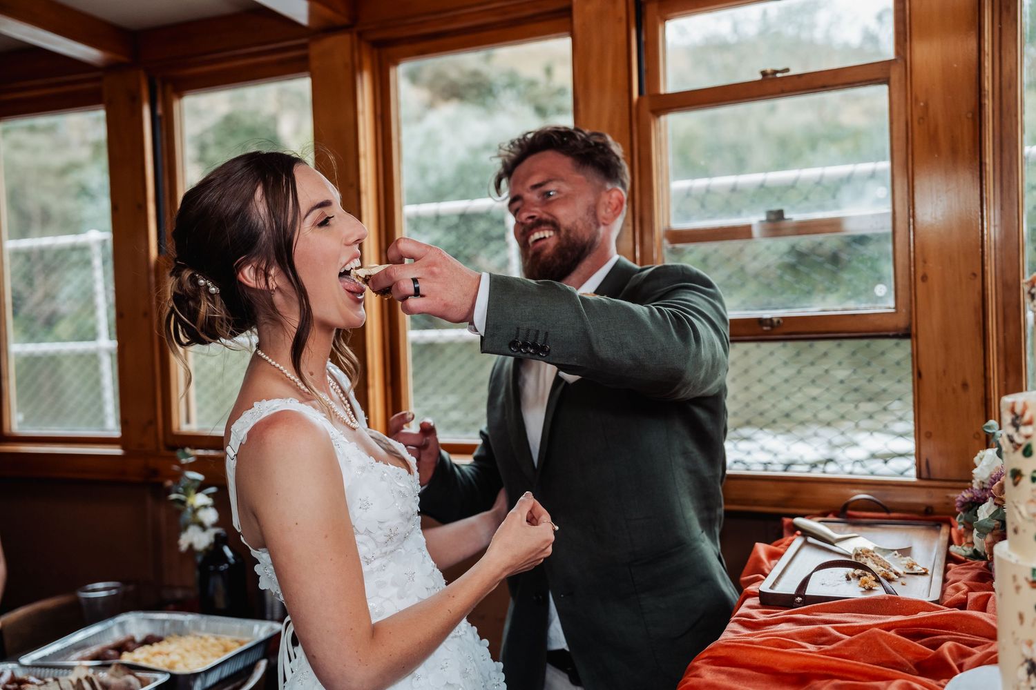 Groom playfully feeding bride during wedding reception on a boat venue.