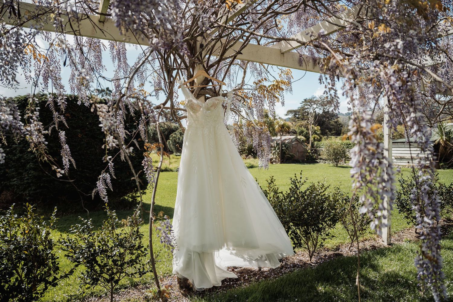 White wedding shoes arranged artistically on grass beneath flowering trees in an outdoor garden setting.