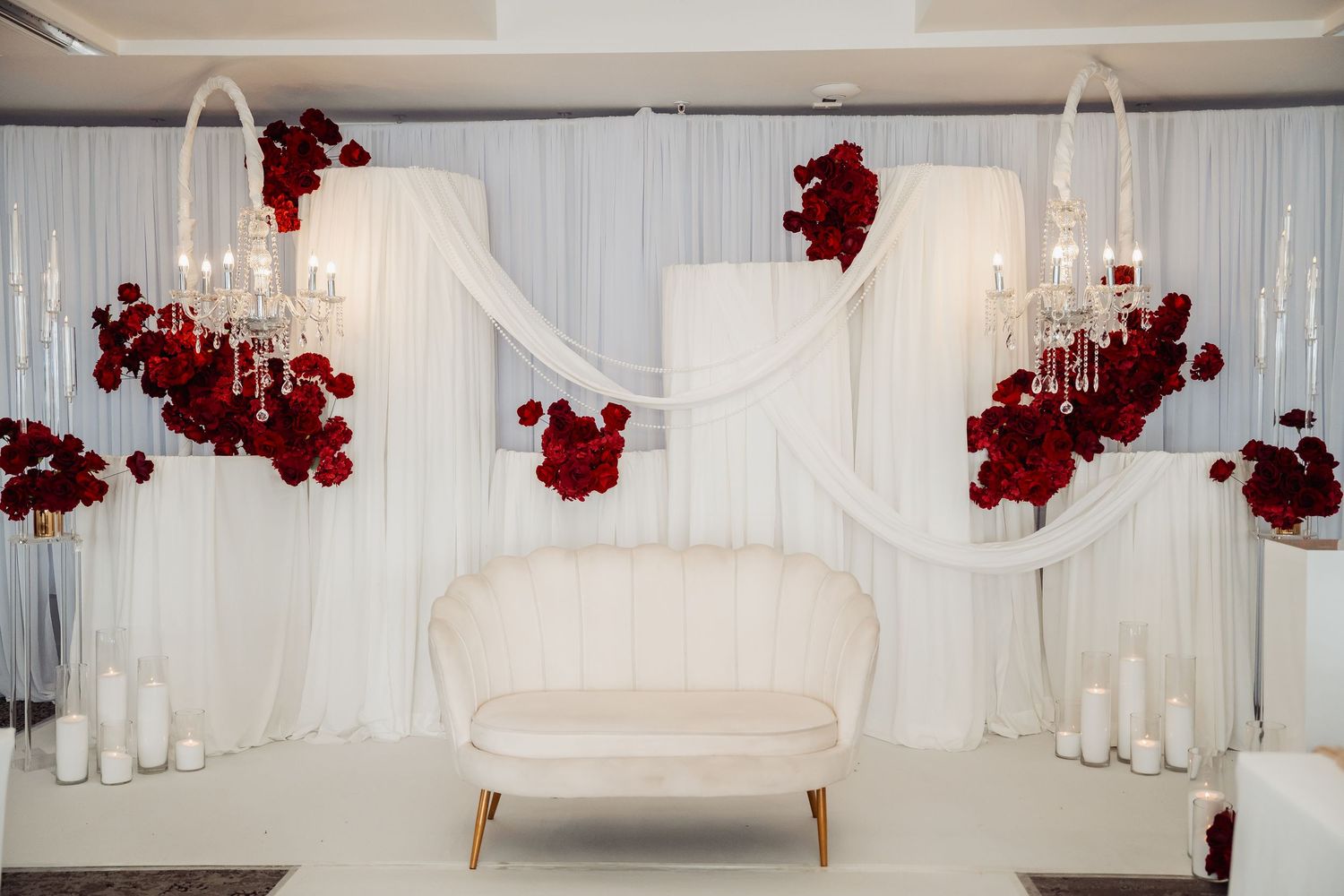 White wedding backdrop decorated with cascading deep red roses and drapery.