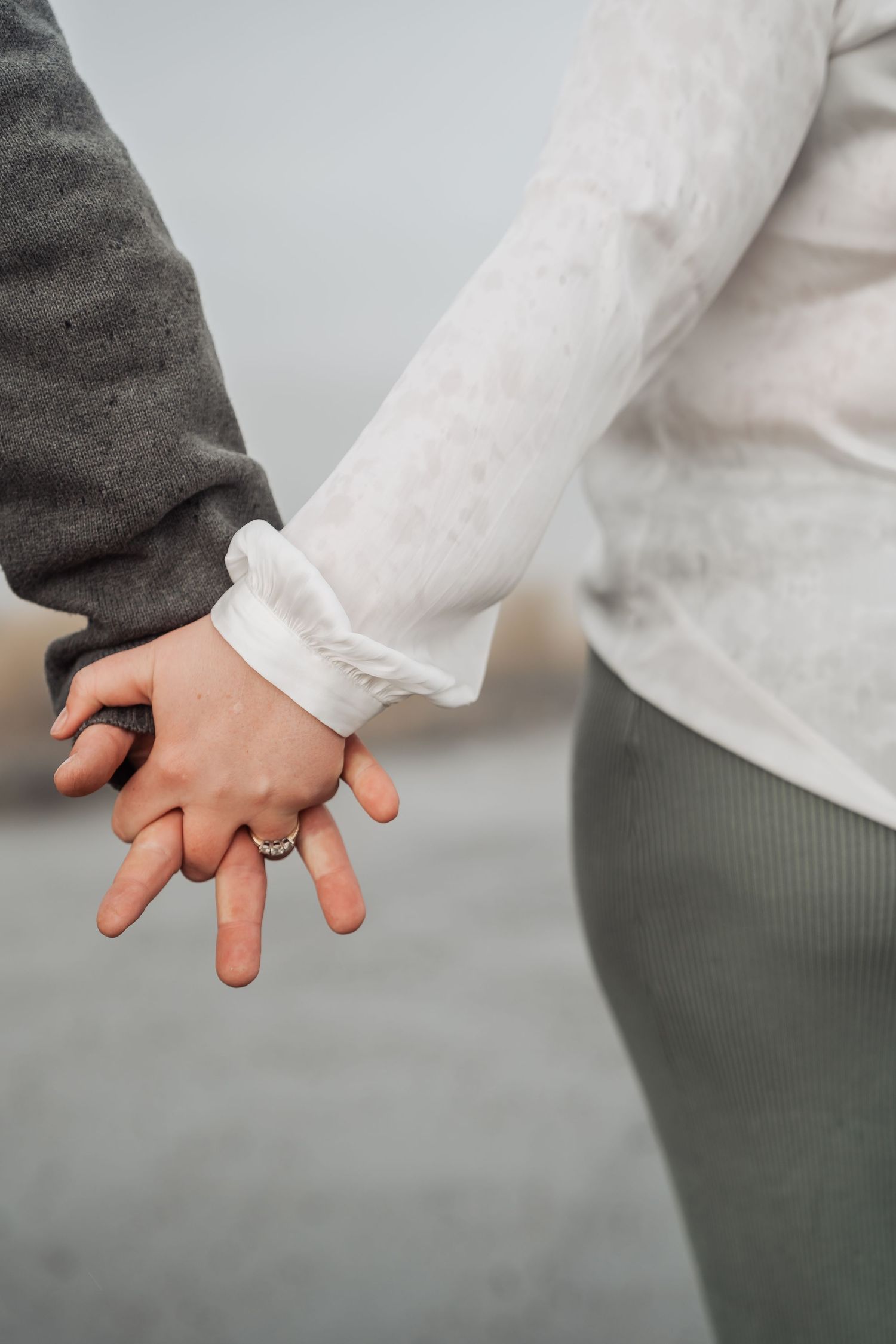 Close up of two hands holding each other with one person wearing a ring against a gray background.