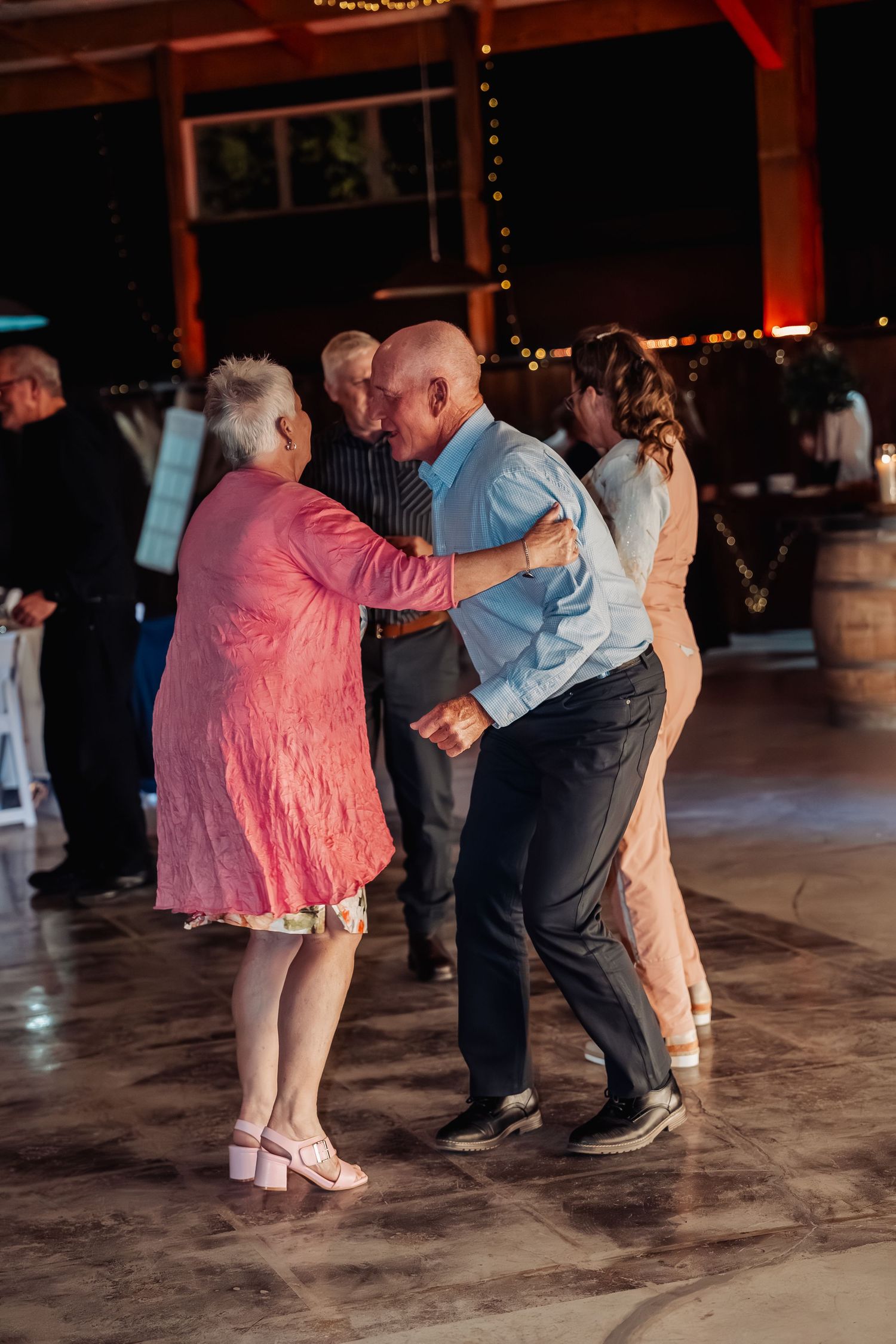 Elderly couple dancing together on a warmly lit dance floor at a wedding reception.