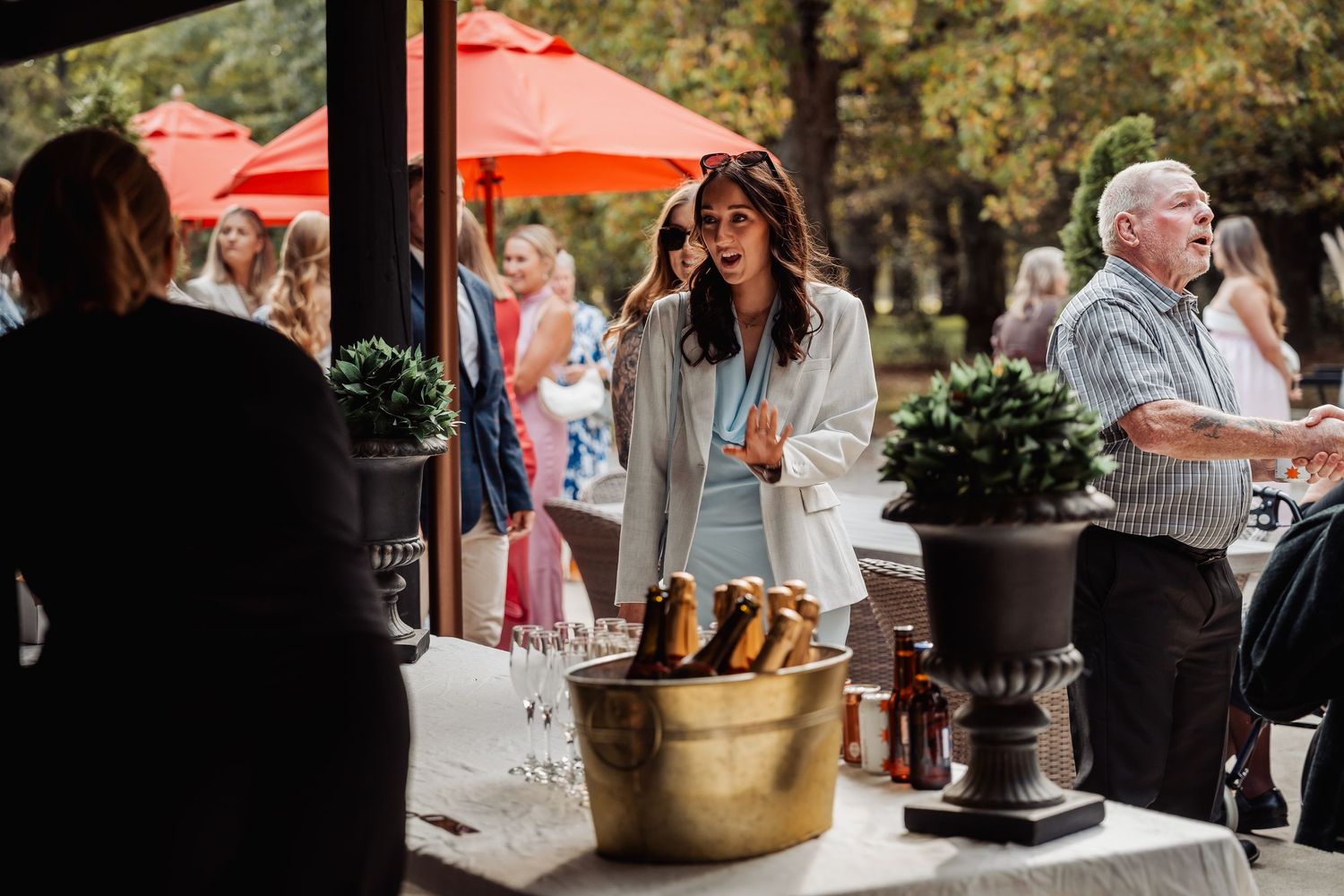 Wedding guest laughing outdoors at sunny fall reception with red umbrellas.