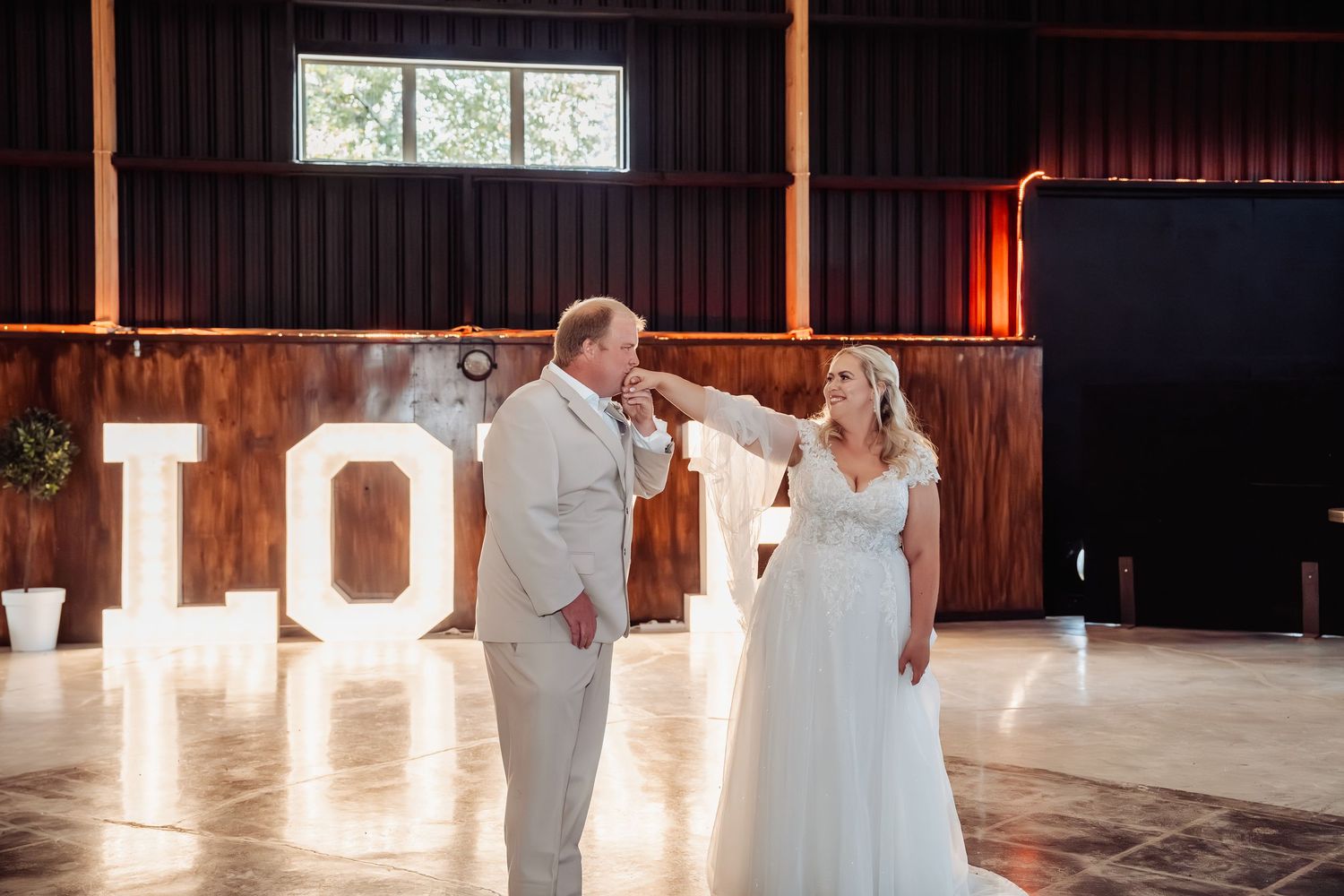 Bride and groom share a joyful moment on the dance floor in front of illuminated LOVE letters in a barn wedding venue.