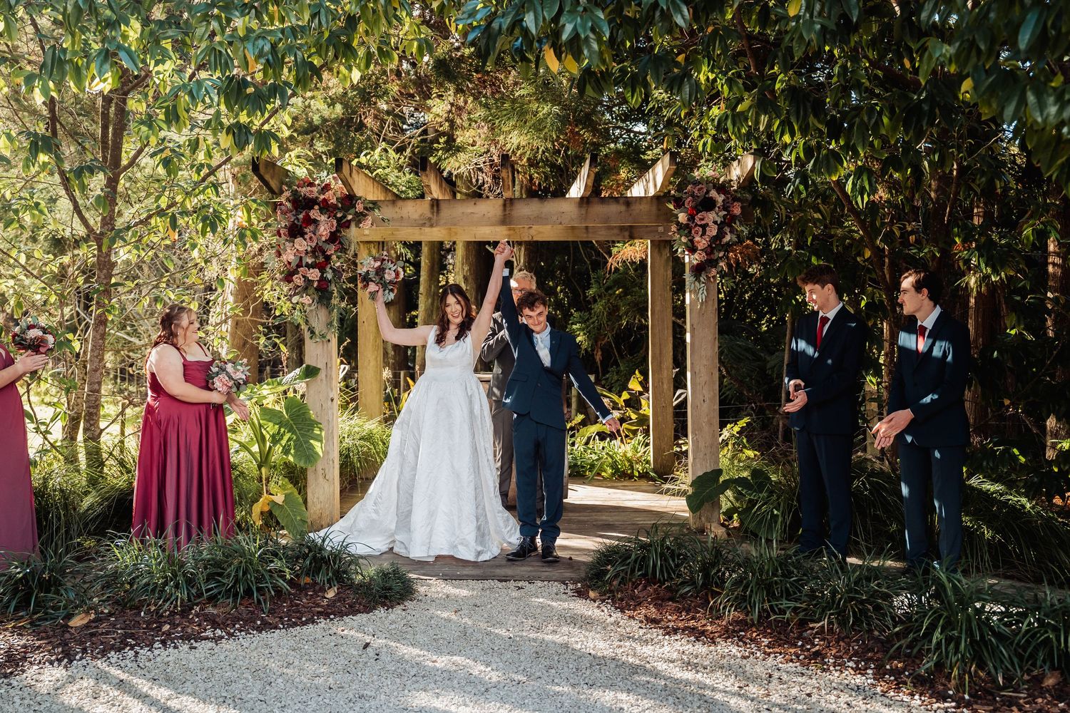 Bride and groom celebrating under floral arch at outdoor garden wedding ceremony with guests.