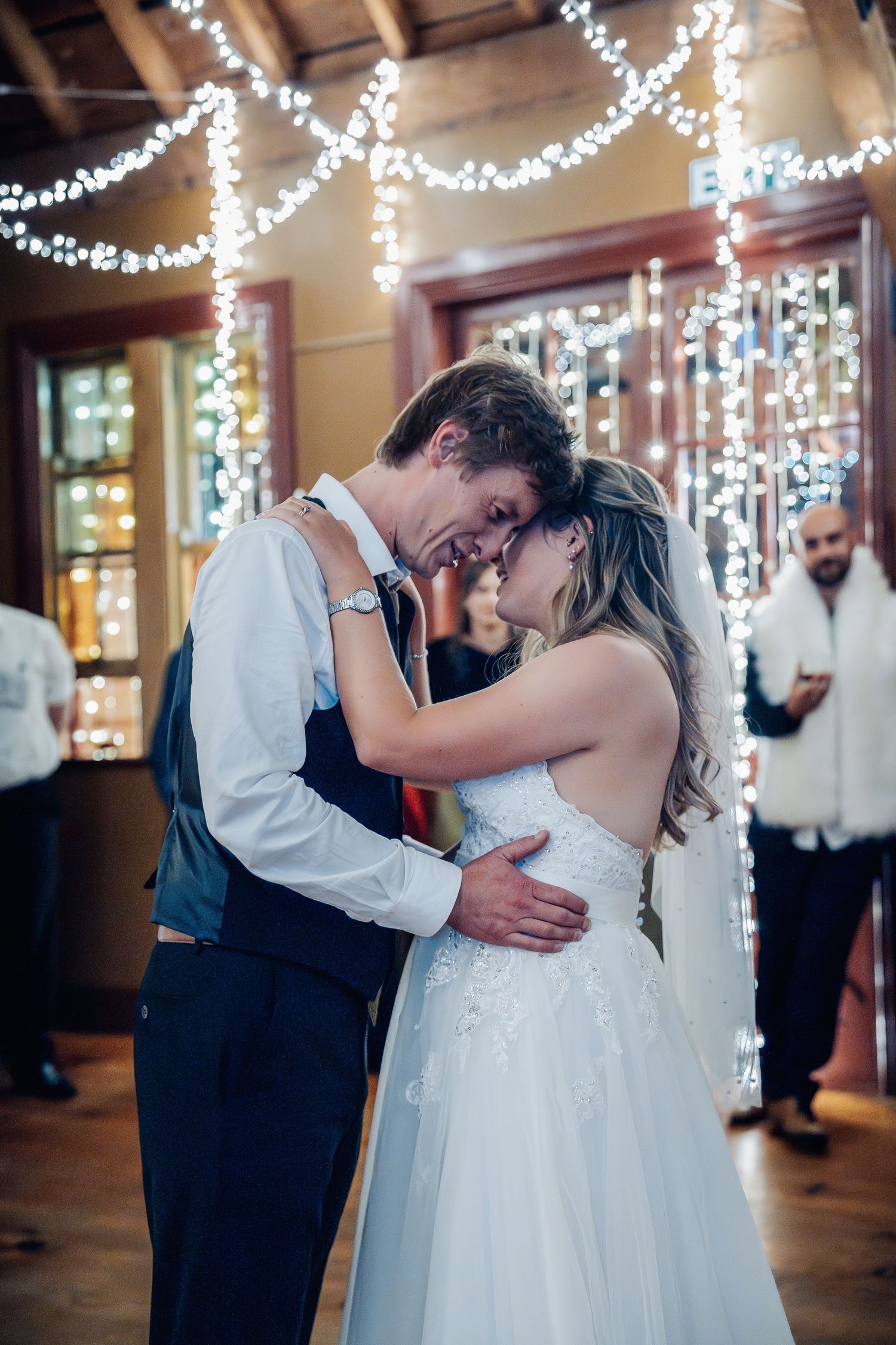 A couple shares an intimate moment during their first dance under twinkling fairy lights at their wedding reception.