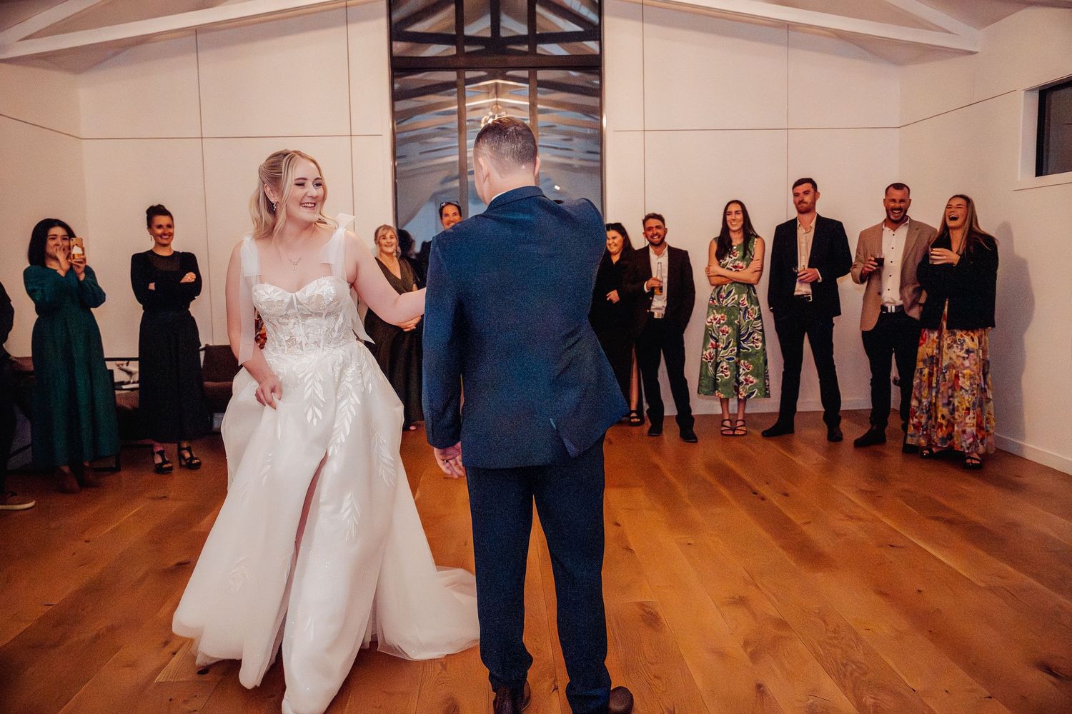 Wedding reception dance in elegant venue with hardwood floors and white walls.