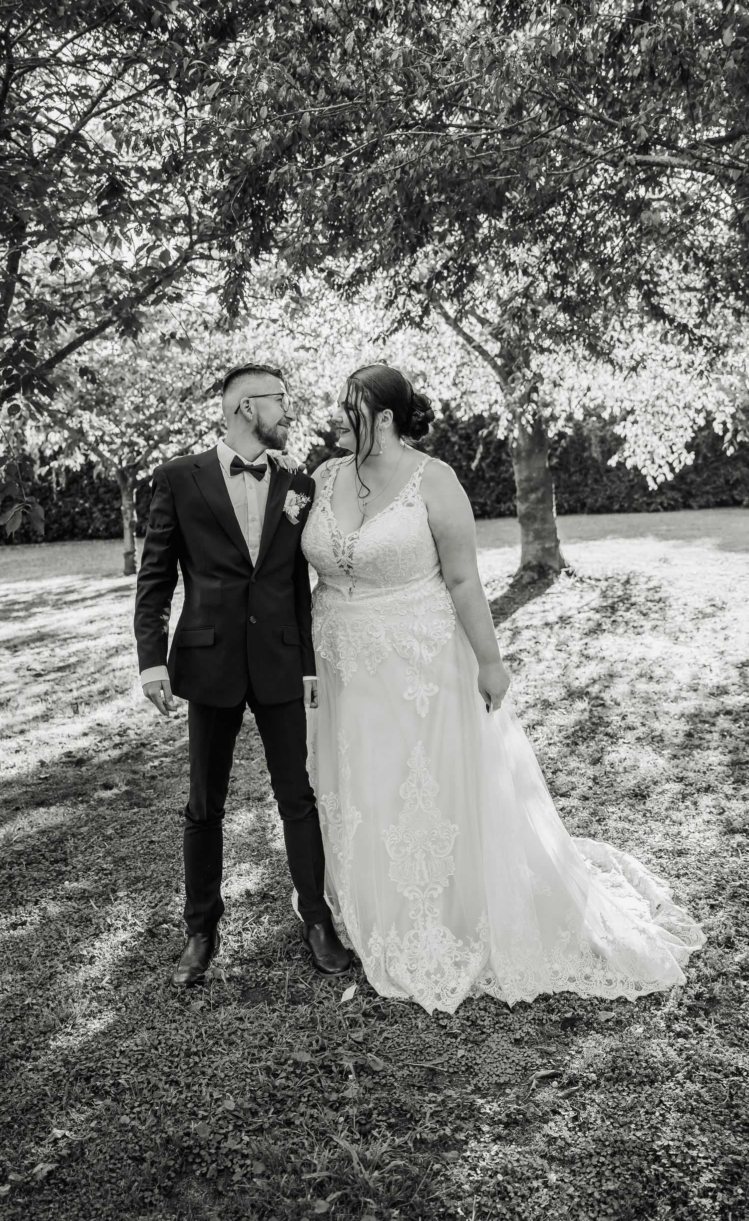 A black and white wedding portrait taken under trees in a garden setting.