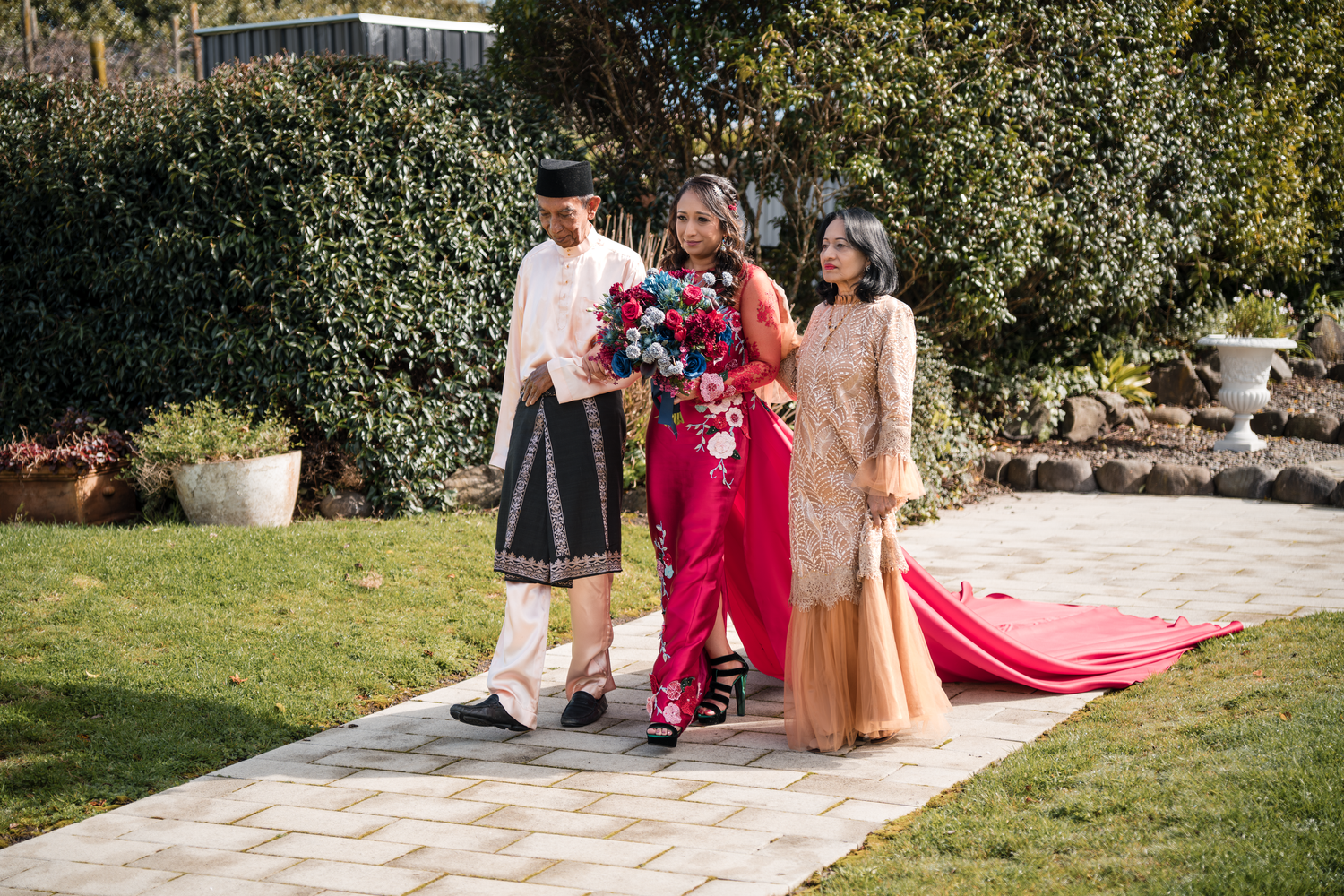 Wedding party wearing fusion of traditional and modern outfits pose on garden pathway.