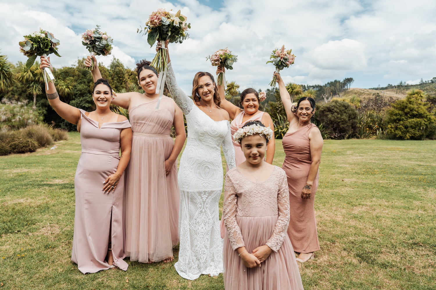 Wedding party in blush pink dresses pose together on a hillside with bouquets.