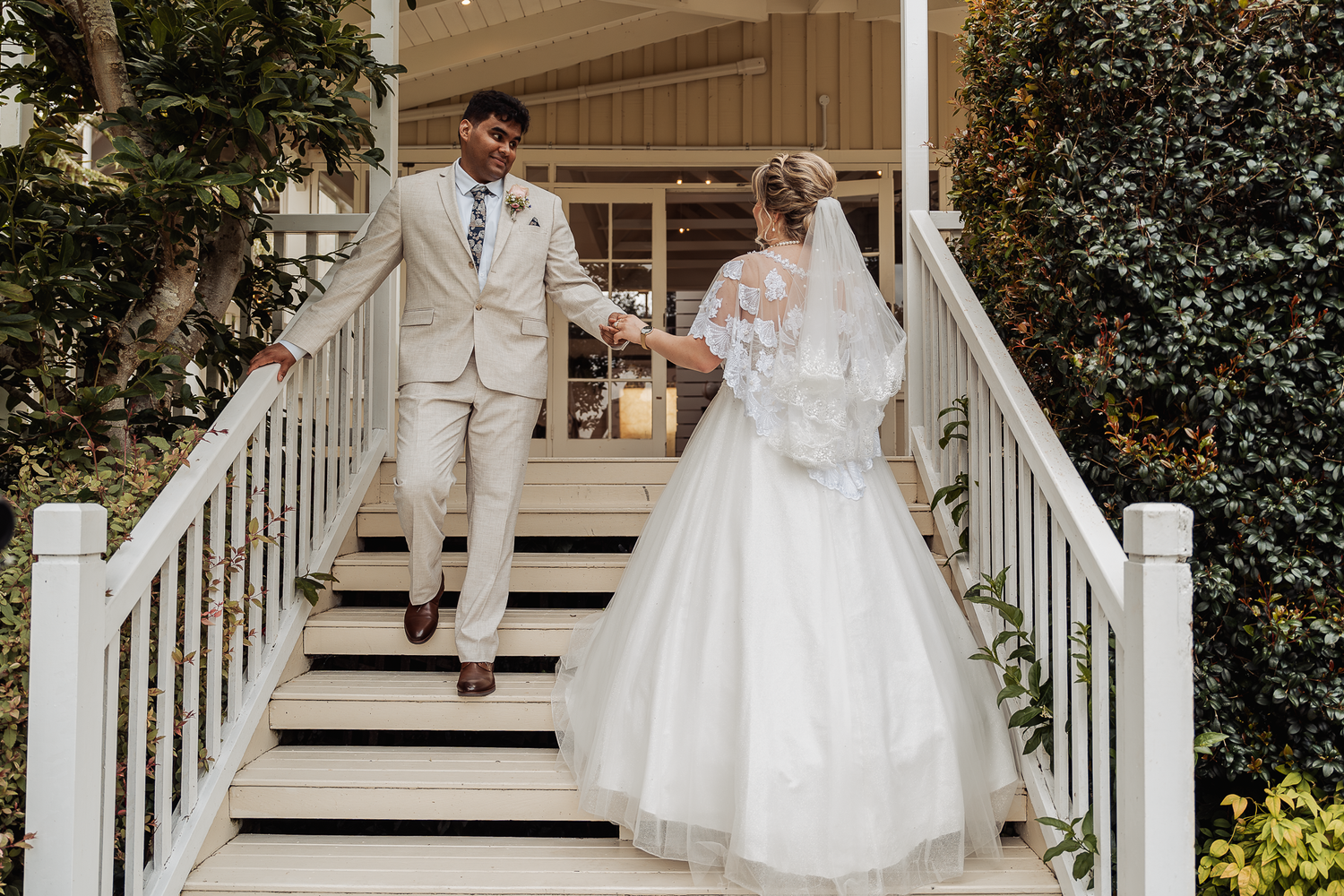 Newlyweds descend white stairs of wedding venue in elegant attire.