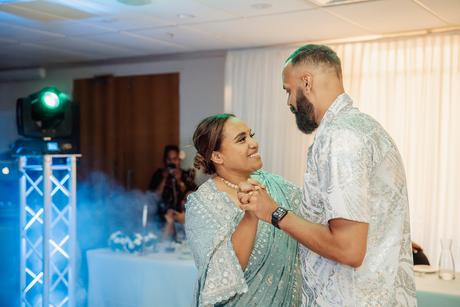 A couple sharing a romantic dance moment at a wedding reception with blue lighting.