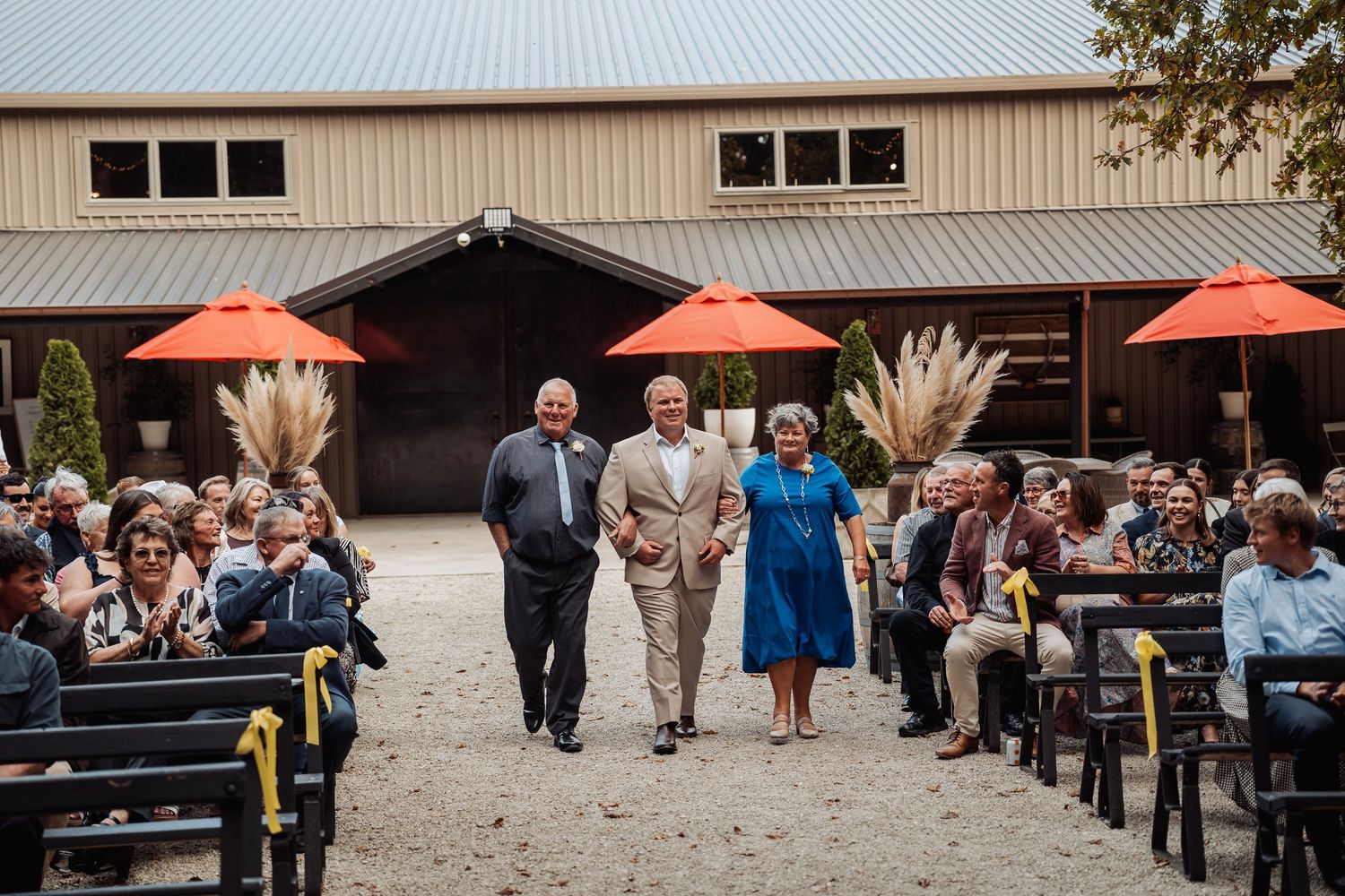 Elegantly dressed guests attend an outdoor wedding ceremony at a rustic barn venue.