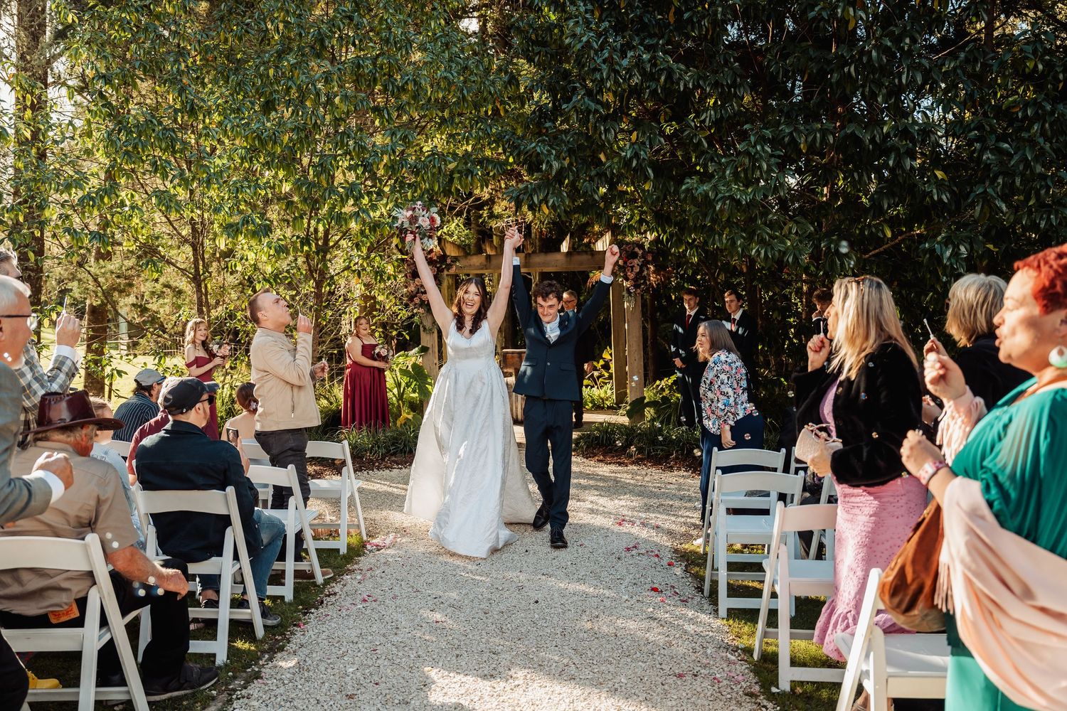 Bride and groom celebrate joyfully walking down the aisle at outdoor wedding ceremony.