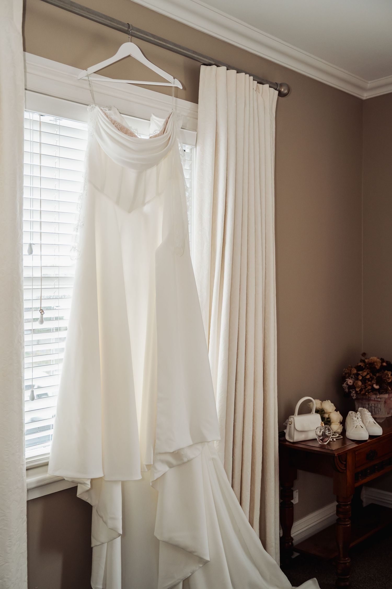 Wedding dress and veil displayed near window with white curtains and natural light.