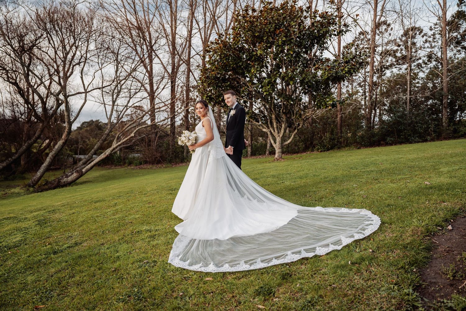 A long wedding dress train spreads elegantly across a manicured garden lawn.