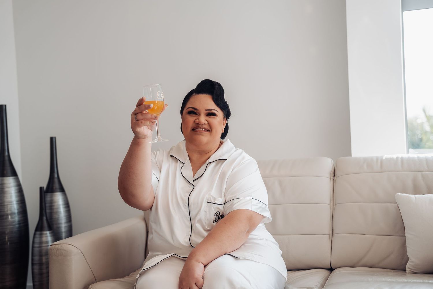 Person sitting comfortably on a beige couch in a bright living room interior, holding what appears to be a snack.