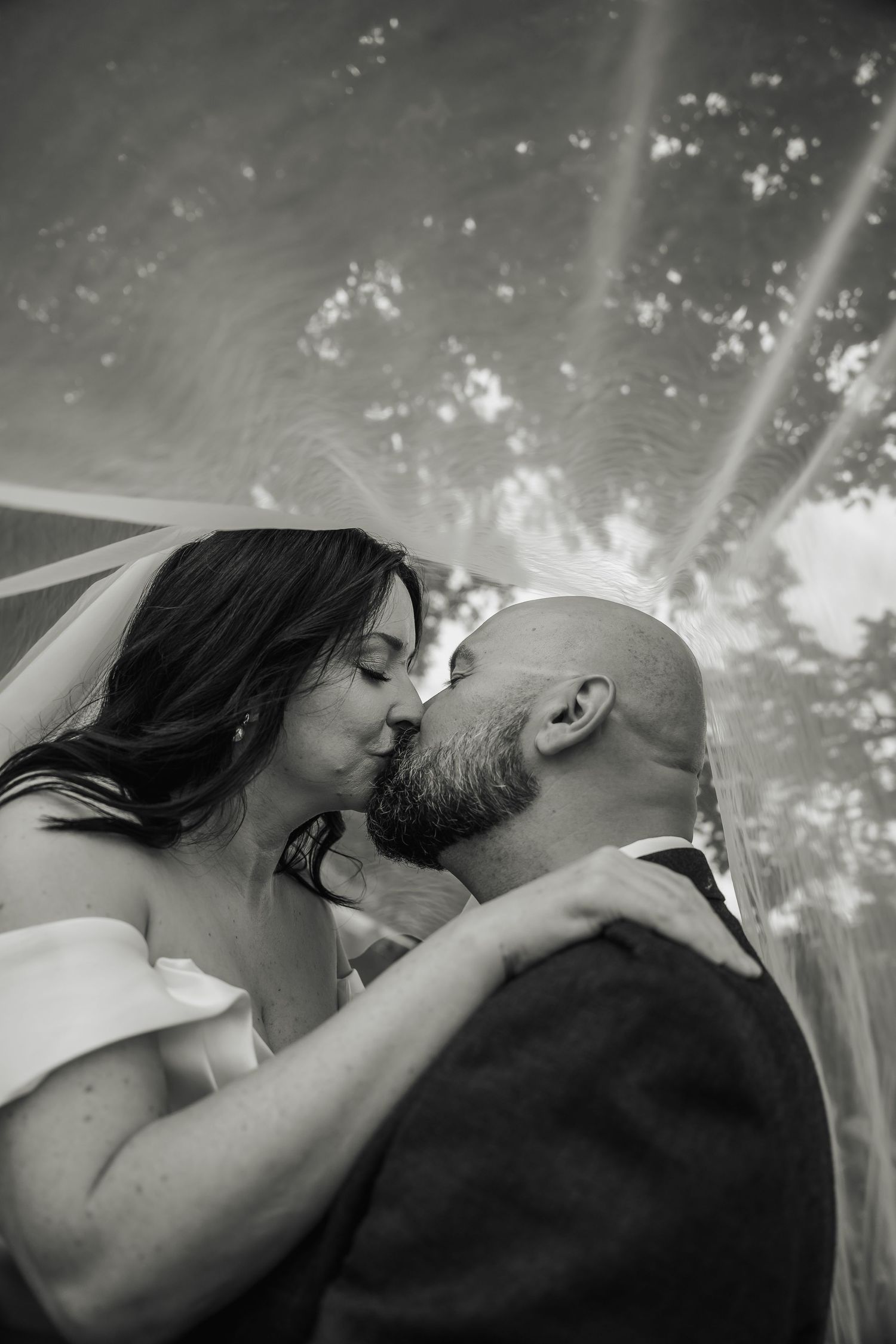 Black and white close-up of bride and groom sharing a passionate kiss beneath the bridal veil.