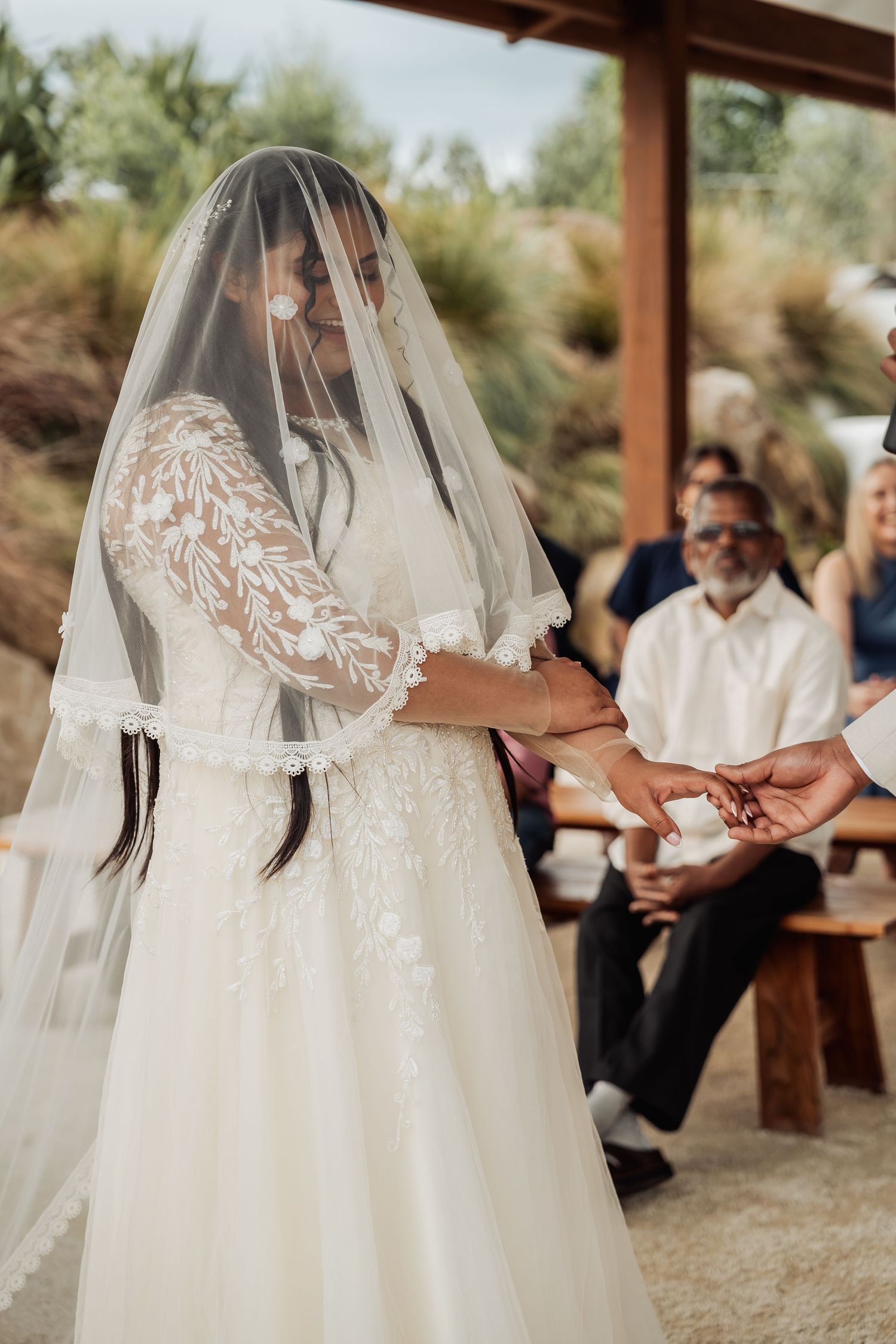 Bride in lace wedding gown exchanging rings during intimate outdoor ceremony.