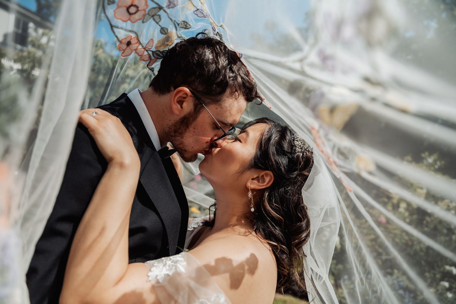 A bride and groom share a romantic kiss under a flowing white veil on their wedding day.