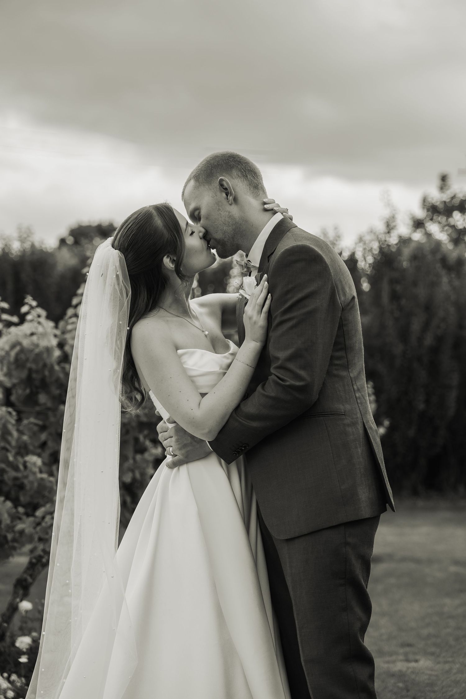 Black and white photo of bride and groom sharing a tender kiss in a garden on their wedding day.