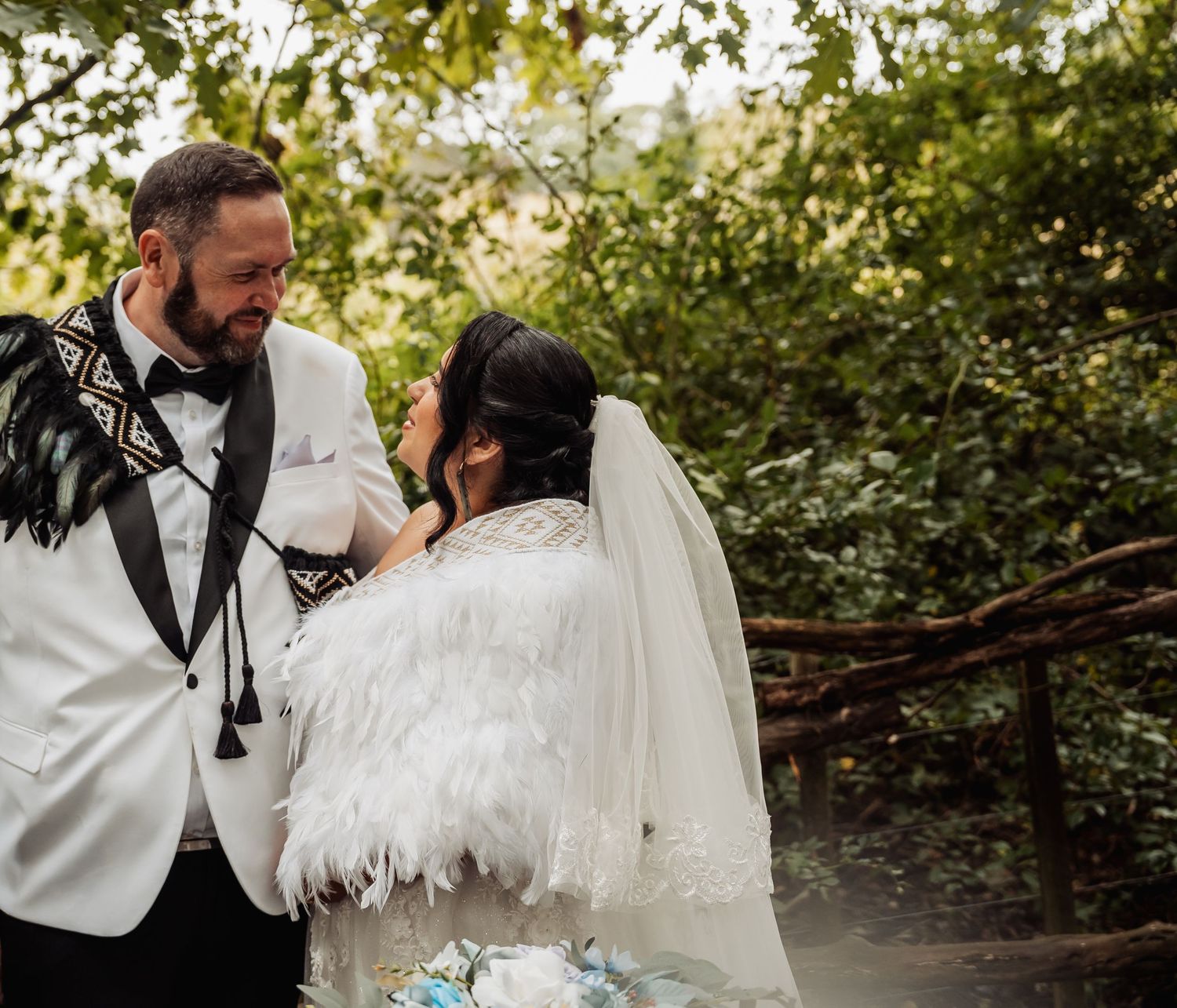 Bride and groom share an intimate moment at outdoor wedding ceremony, bride wearing feathered white wrap and veil.