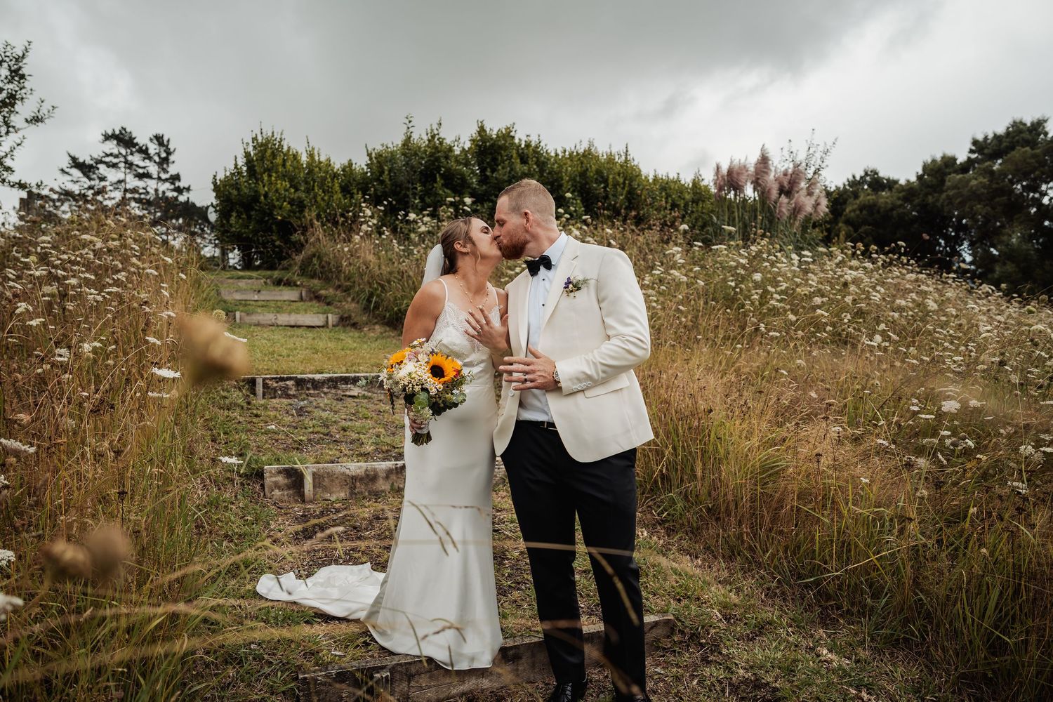 Bride and groom sharing a romantic moment in a wildflower field holding champagne and a sunflower bouquet.