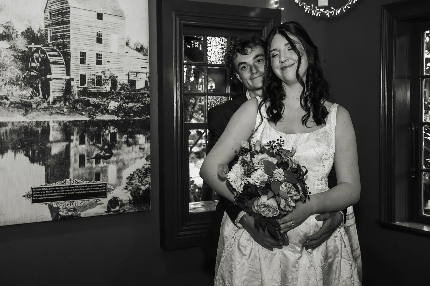 Black and white portrait of bride and groom posing with bouquet in rustic interior.