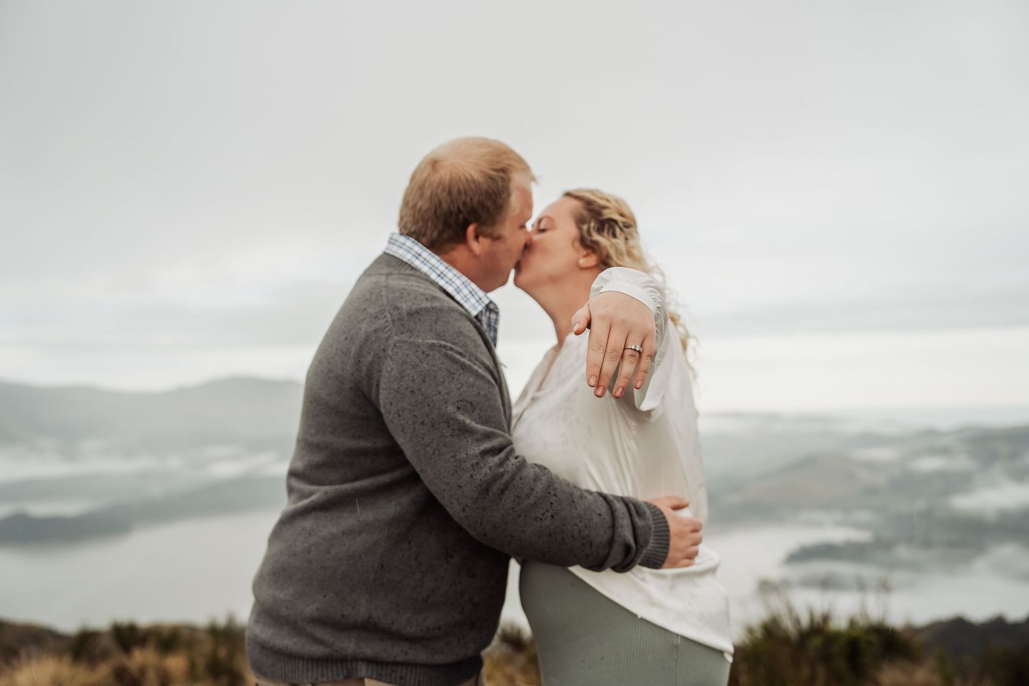 A couple shares a romantic kiss on a cliff overlooking a dramatic stormy ocean on their wedding day.