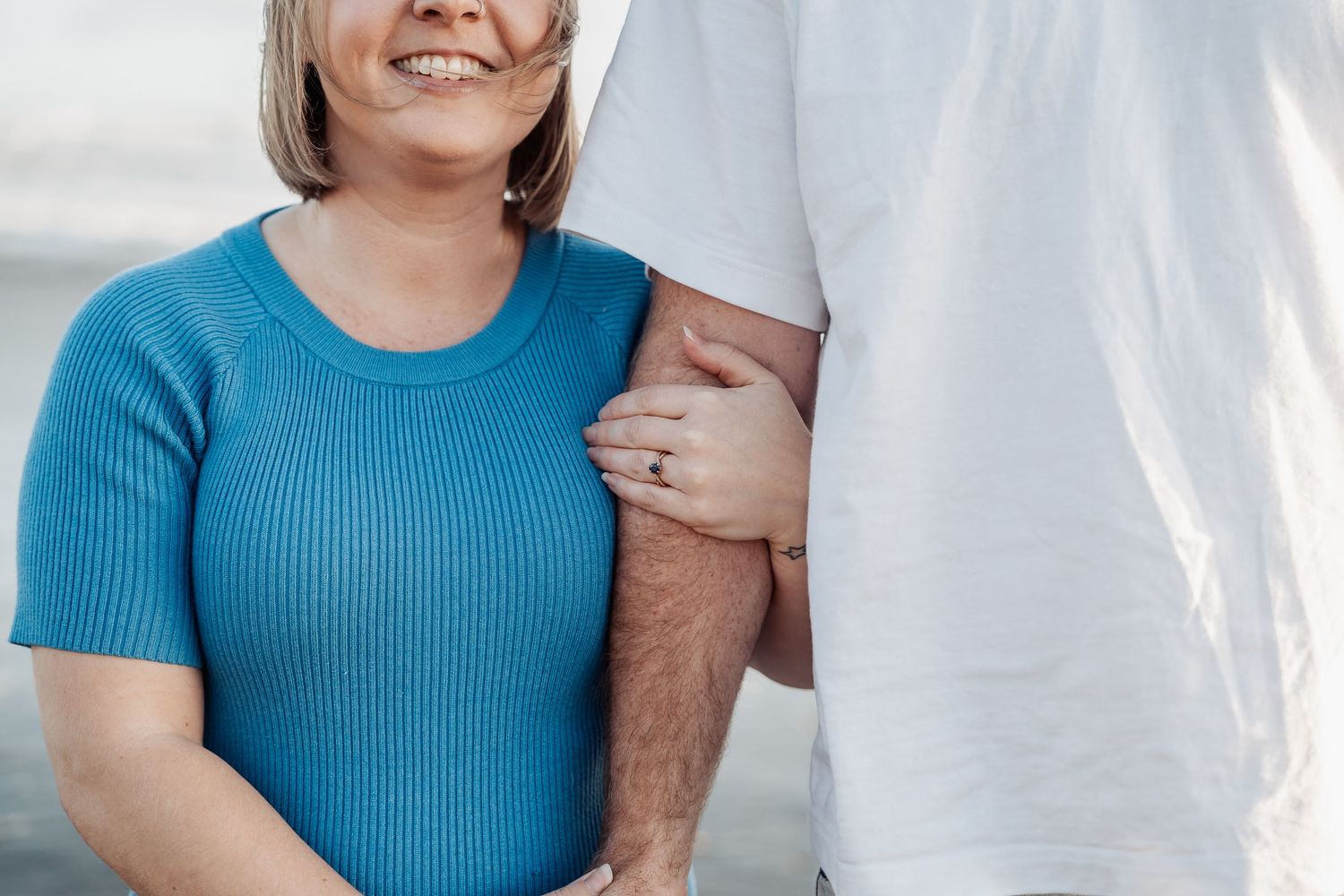 A close-up shot of a couple embracing, with the person in a blue sweater holding their partner's arm.