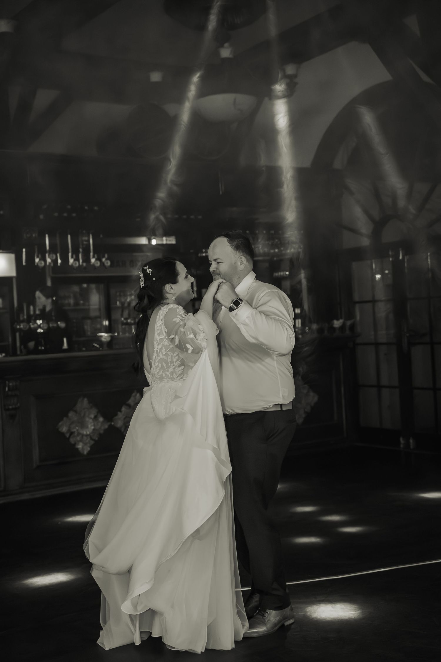 Dramatic black and white dance scene with spotlights illuminating a wedding couple.