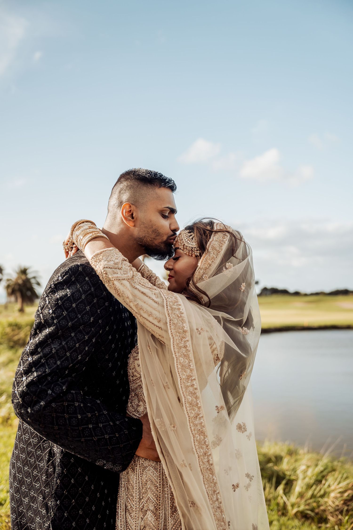 A couple shares a romantic moment by a serene lake during golden hour, wearing coordinating black and beige outfits.