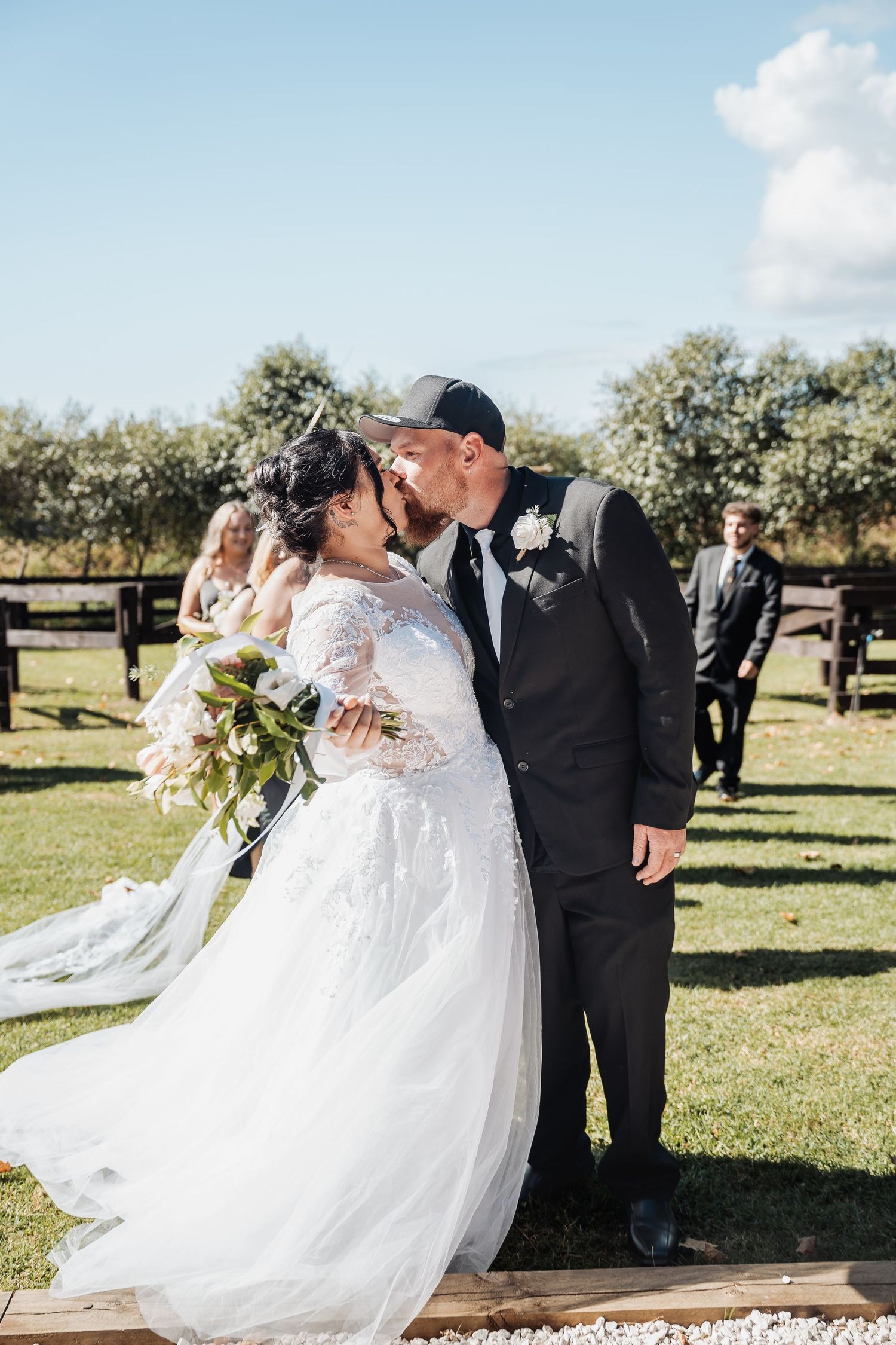 Romantic outdoor wedding ceremony with couple embracing under blue skies surrounded by green trees.