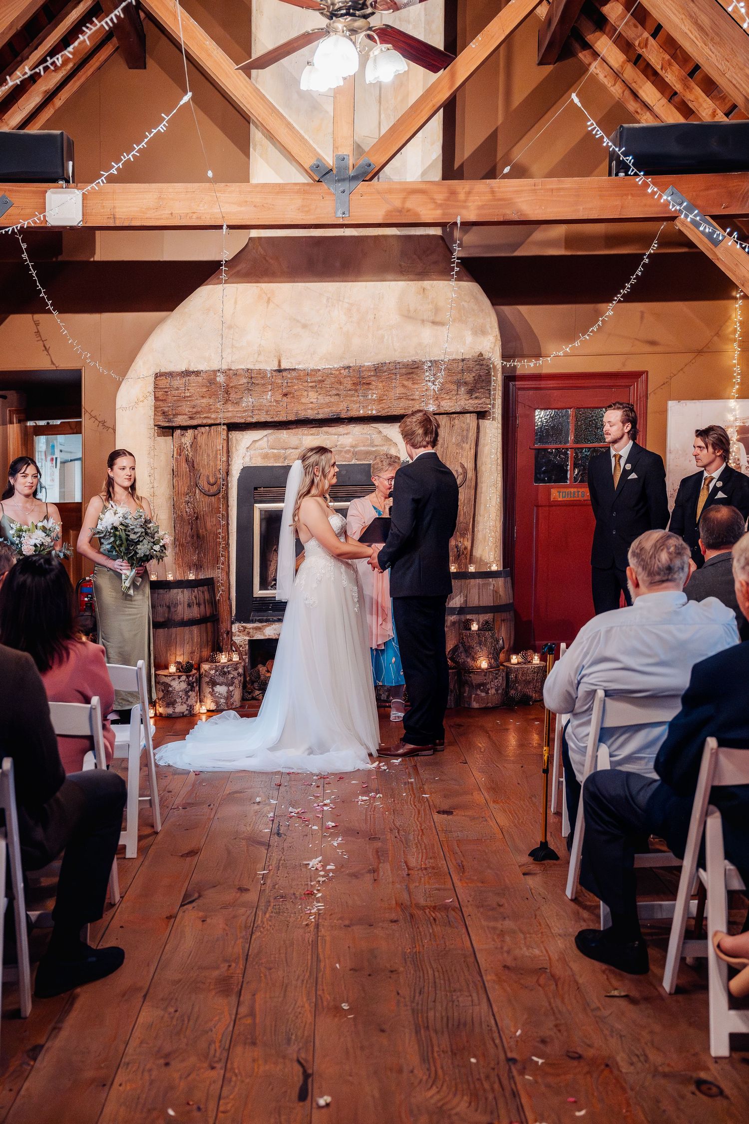 A wedding ceremony taking place in a rustic barn venue with exposed wooden beams and string lights.