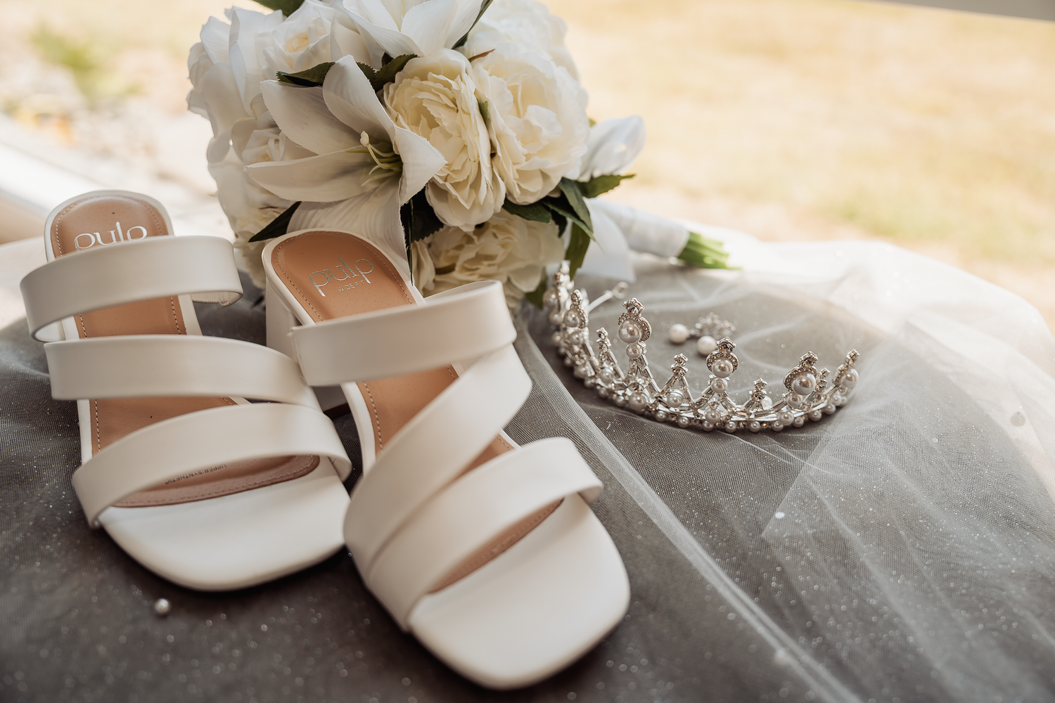Wedding accessories including white strappy sandals, floral bouquet and a delicate tiara.
