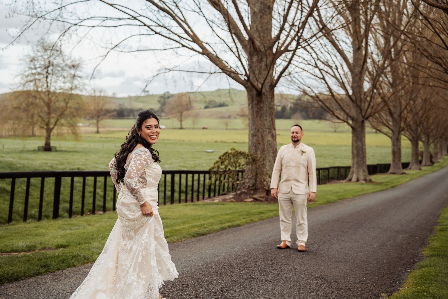 A couple walks along a tree-lined path during their countryside wedding celebration.