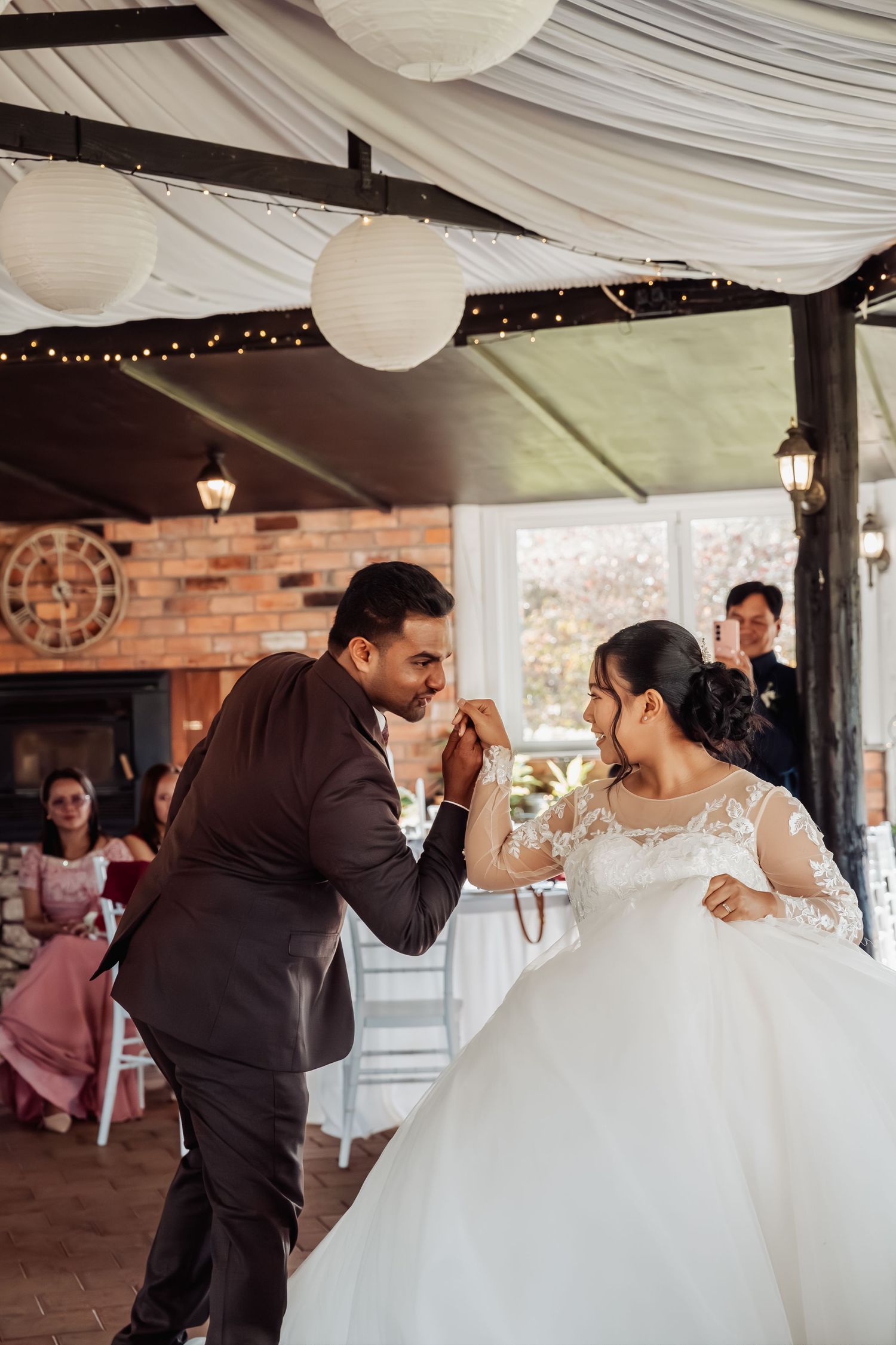 Bride and groom share their first dance under white lanterns in an elegant rustic wedding venue.