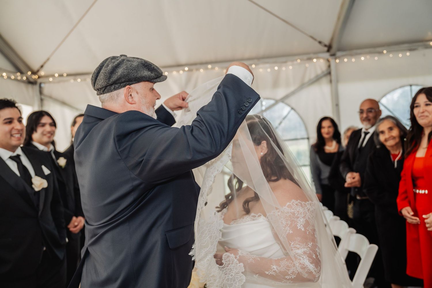 Traditional Jewish wedding ceremony moment with rabbi lifting bride's veil during indoor celebration.