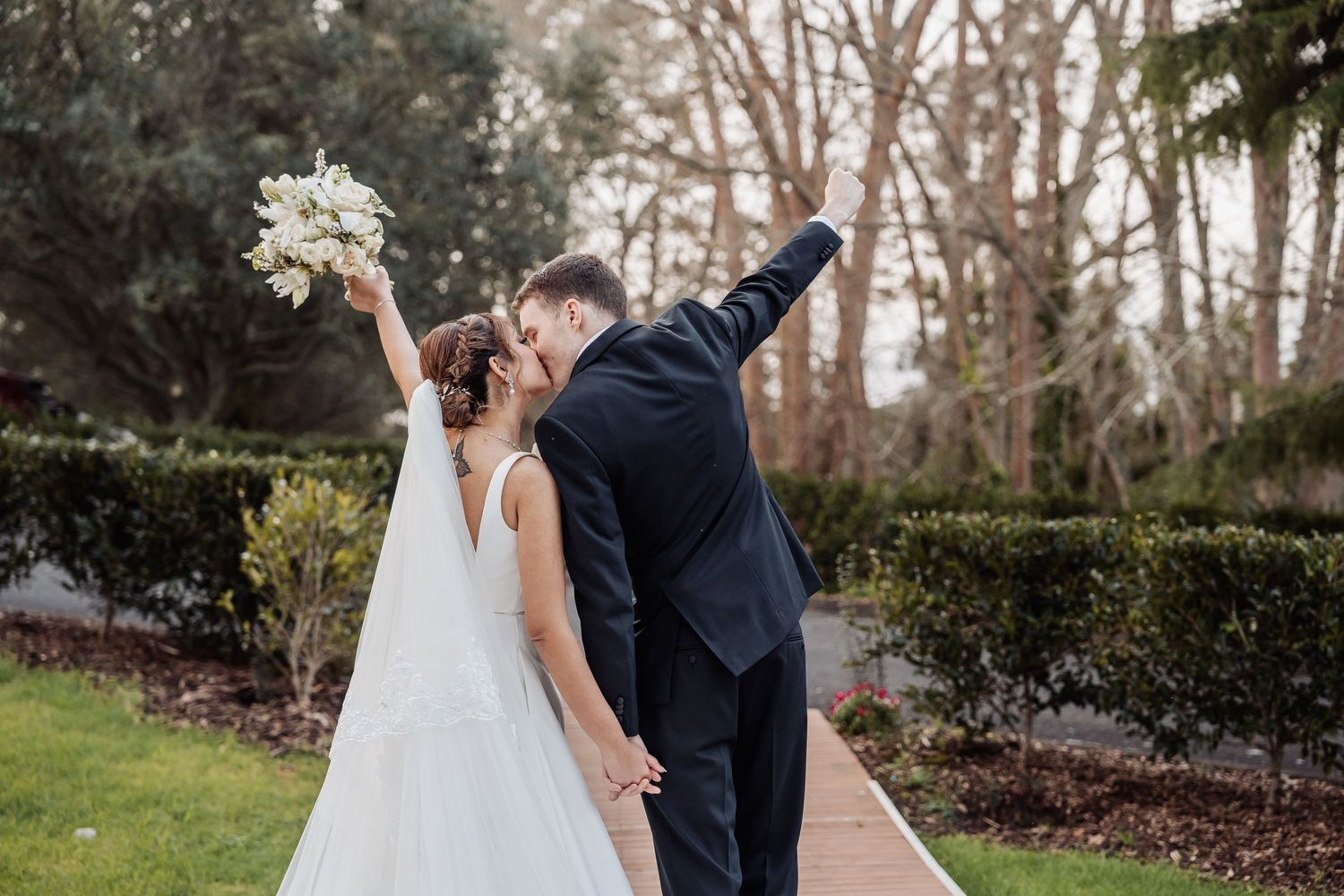Wedding couple photographs captured in a natural outdoor setting with trees and landscaping.