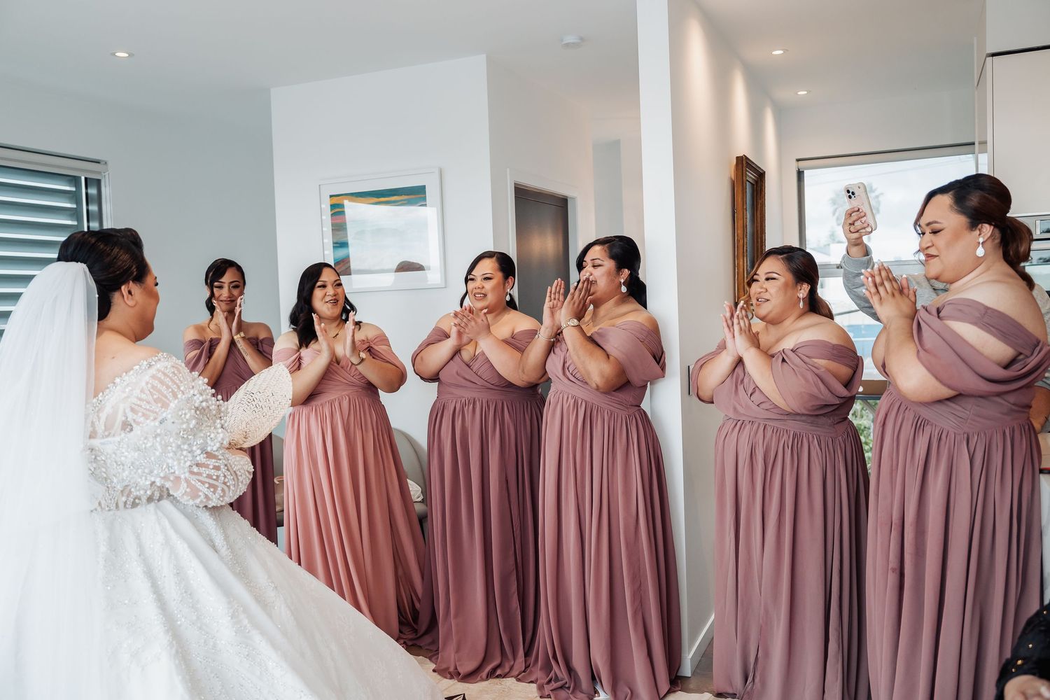 Bridesmaids wearing dusty rose gowns stand in a line showing off their dresses.