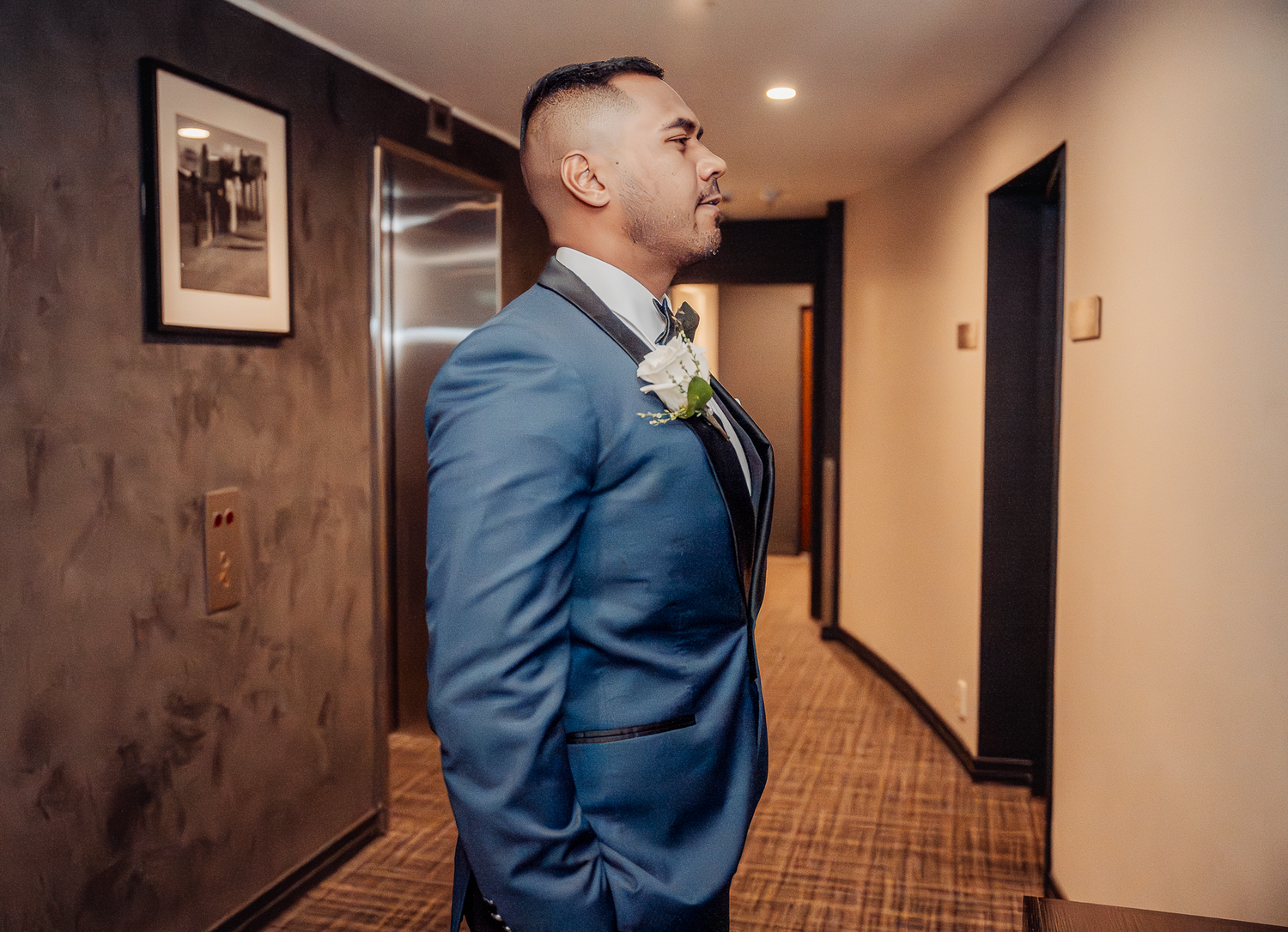 Groom in blue suit stands confidently in hotel hallway before ceremony.