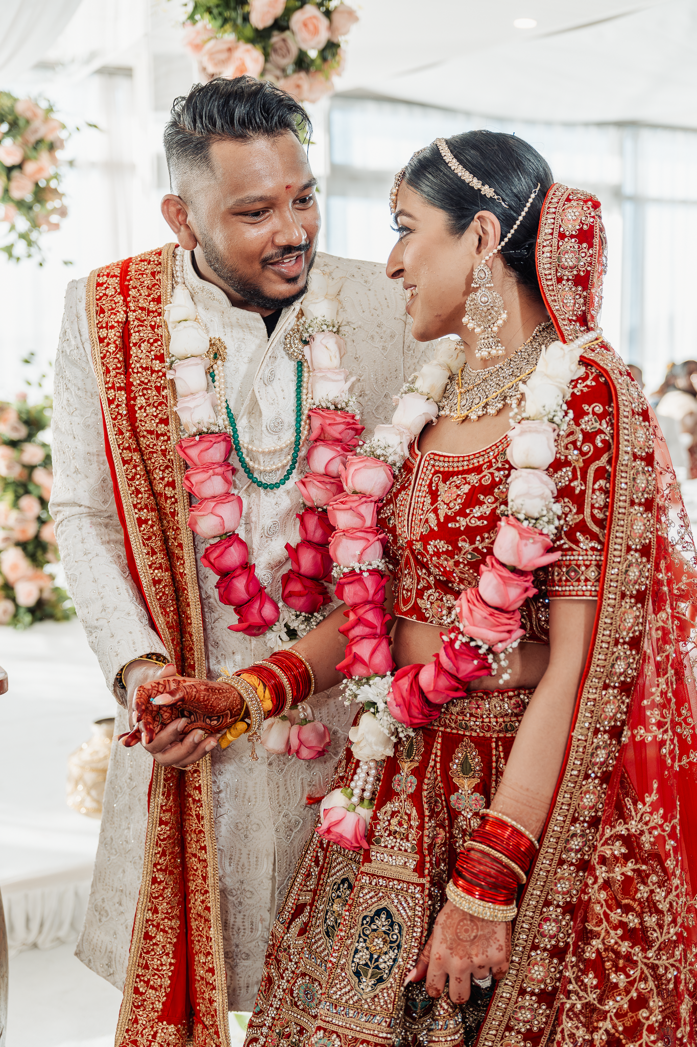 Traditional Indian wedding couple wearing ornate red and gold attire with floral garlands.