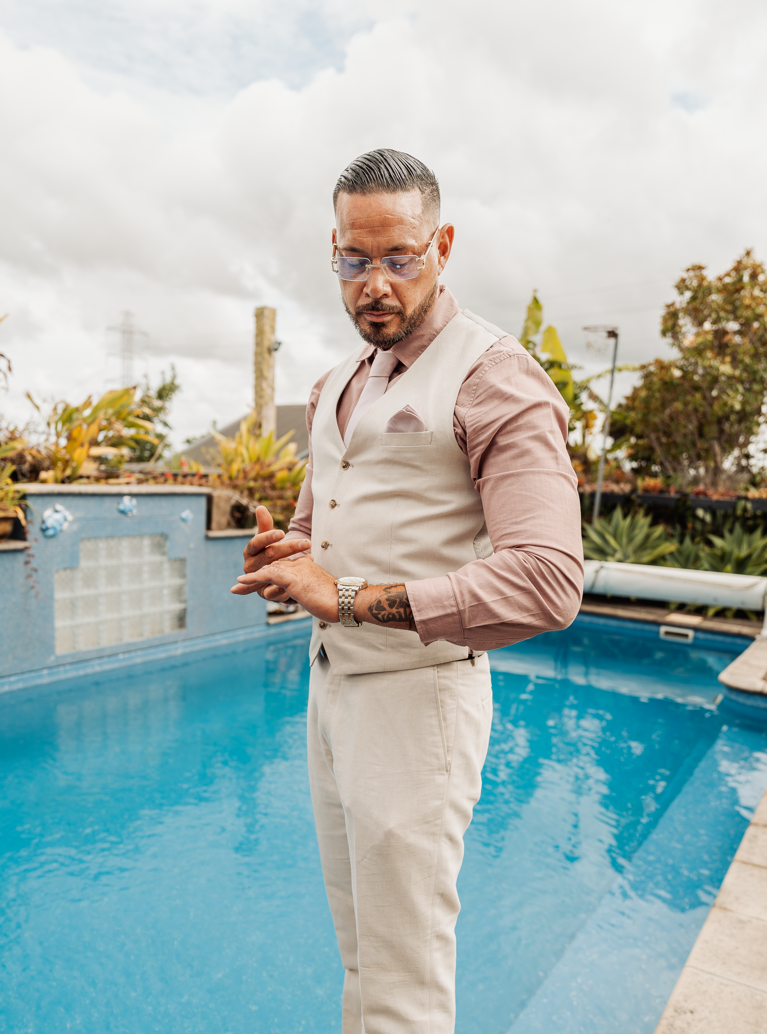 Person in light beige suit checks phone by blue swimming pool.