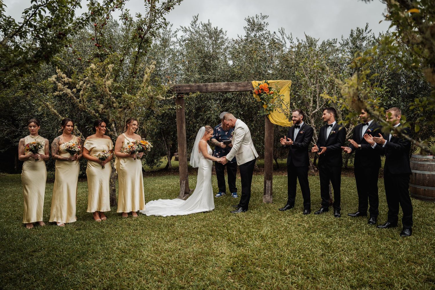 Wedding party gathered at a rustic outdoor altar with sunflower decorations during the ceremony.