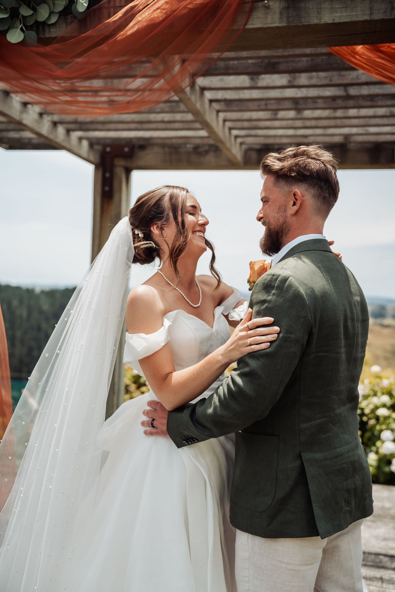 Bride and groom embracing and smiling at each other during an outdoor wedding ceremony.