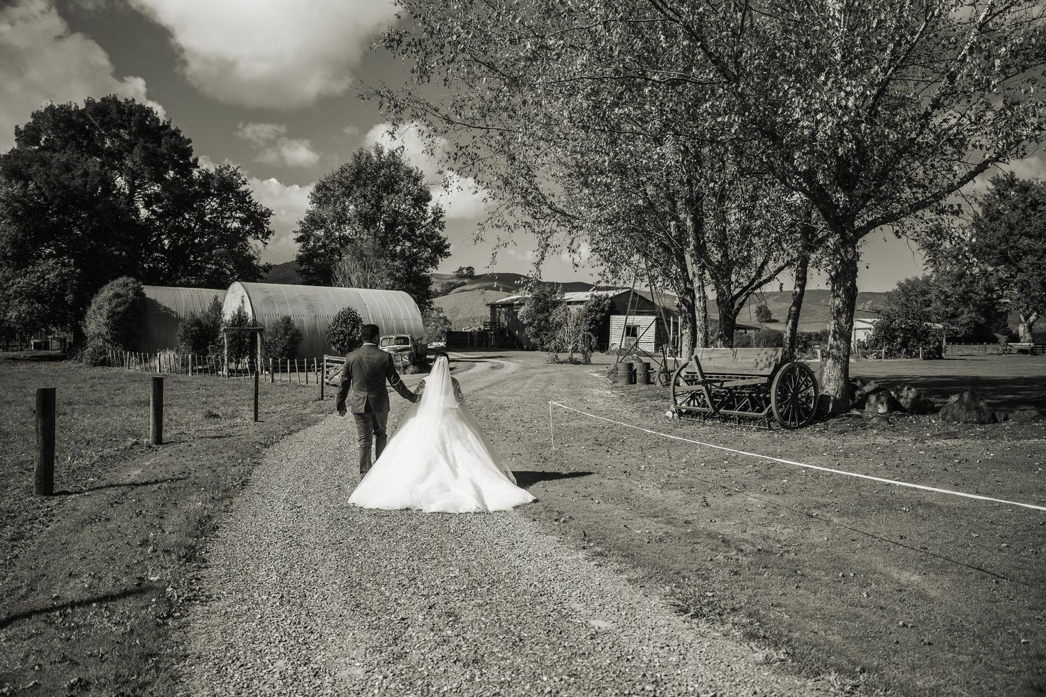 Black and white photo of bride and groom walking along a rural farm pathway.