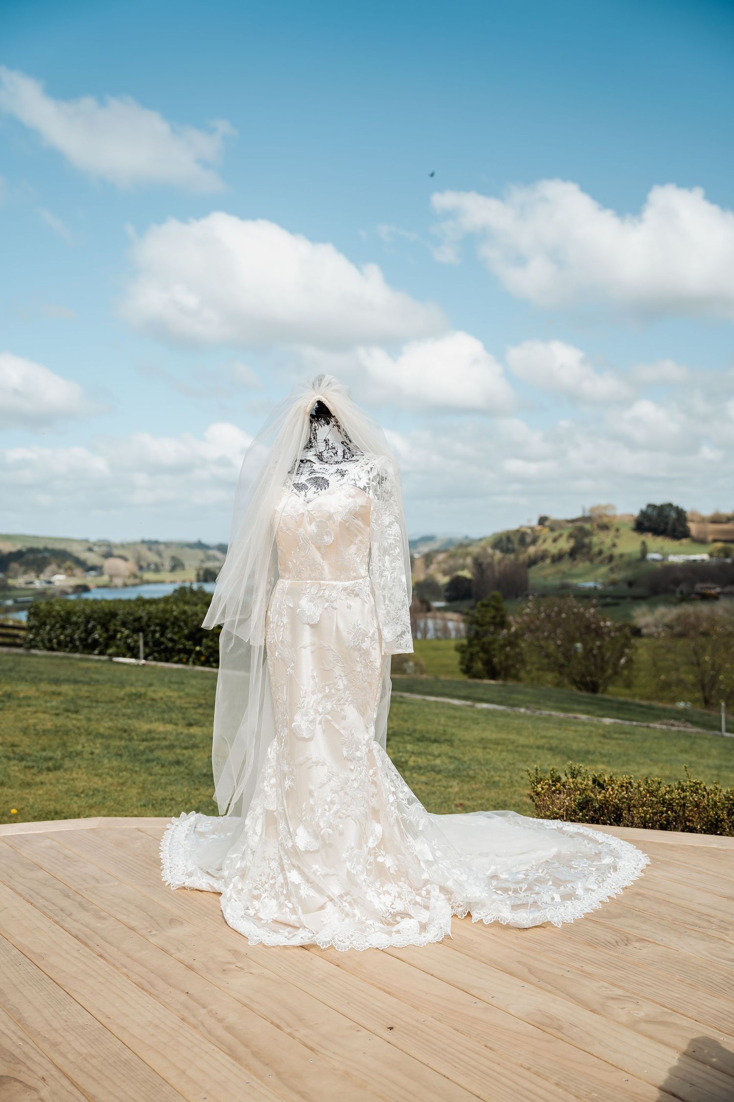 A beautiful lace wedding veil flows elegantly across a wooden deck with rolling green hills in the background.