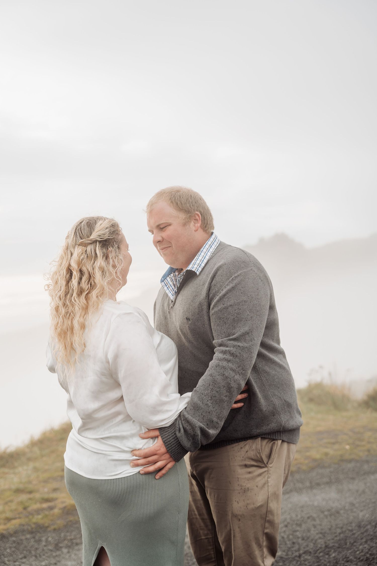 Couple embraces on foggy hilltop during romantic outdoor photoshoot in scenic mountainous landscape.