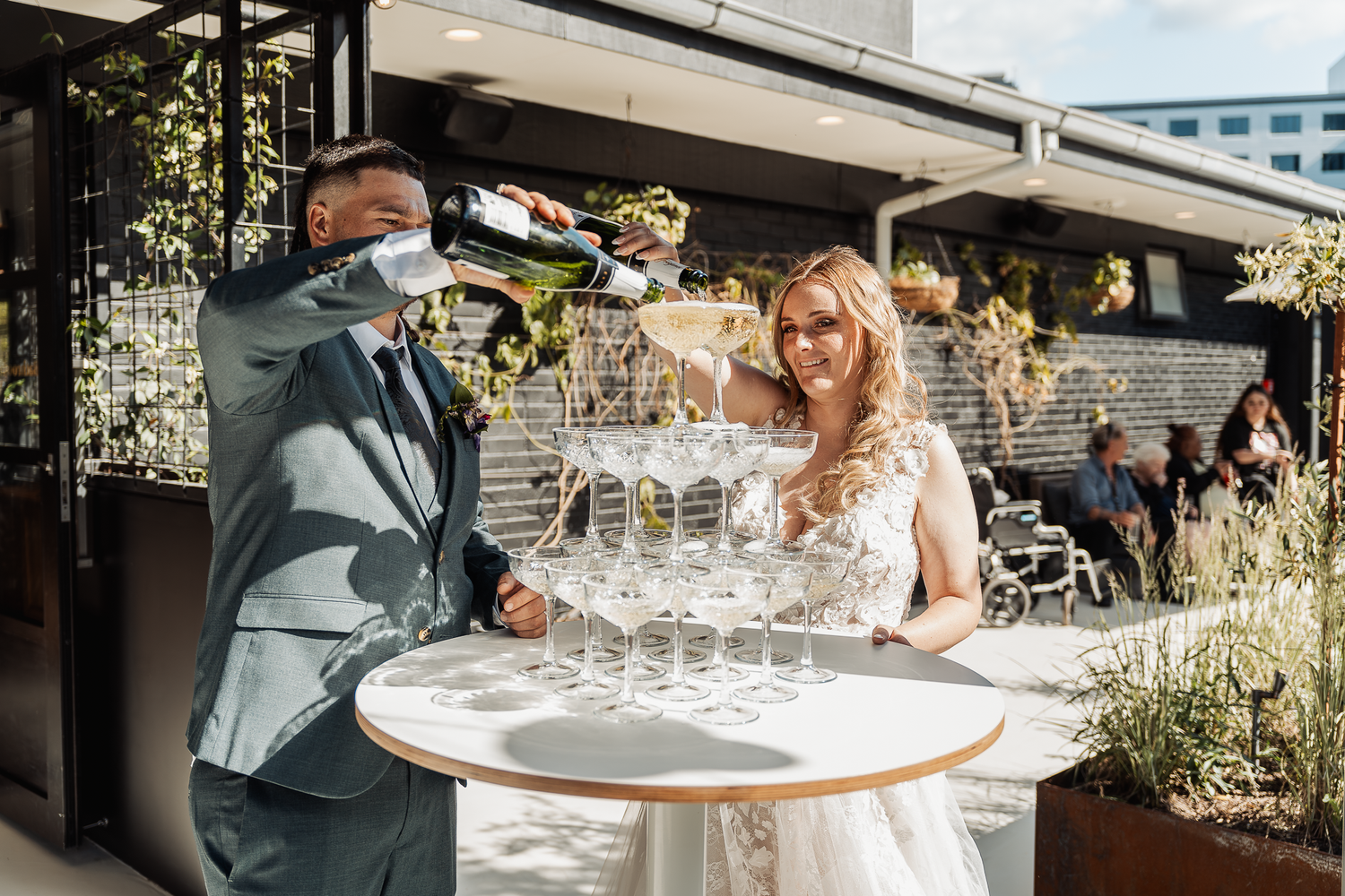 Wedding couple at outdoor reception table with champagne tower.