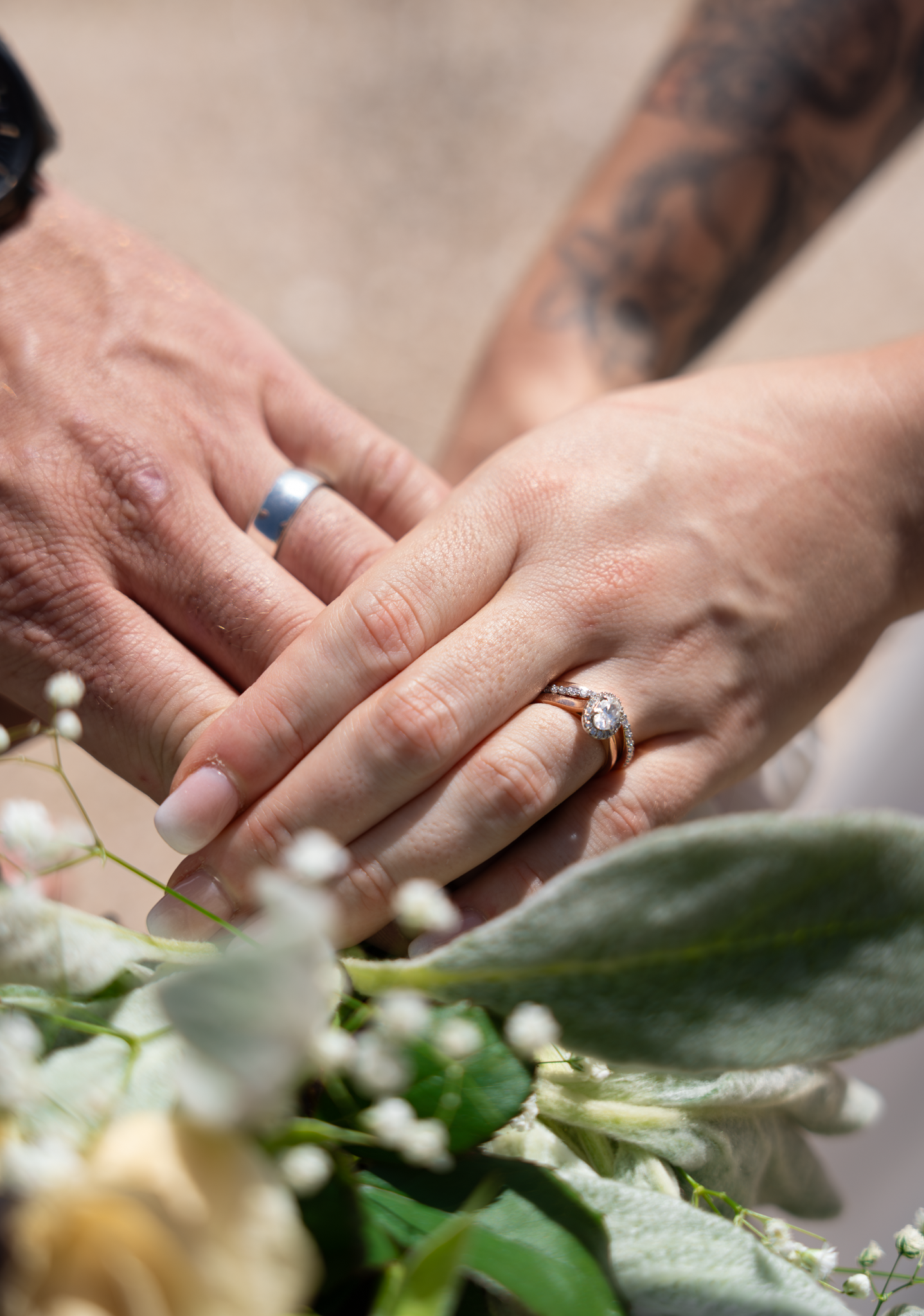 Close-up of hands wearing wedding rings resting on white floral bouquet.