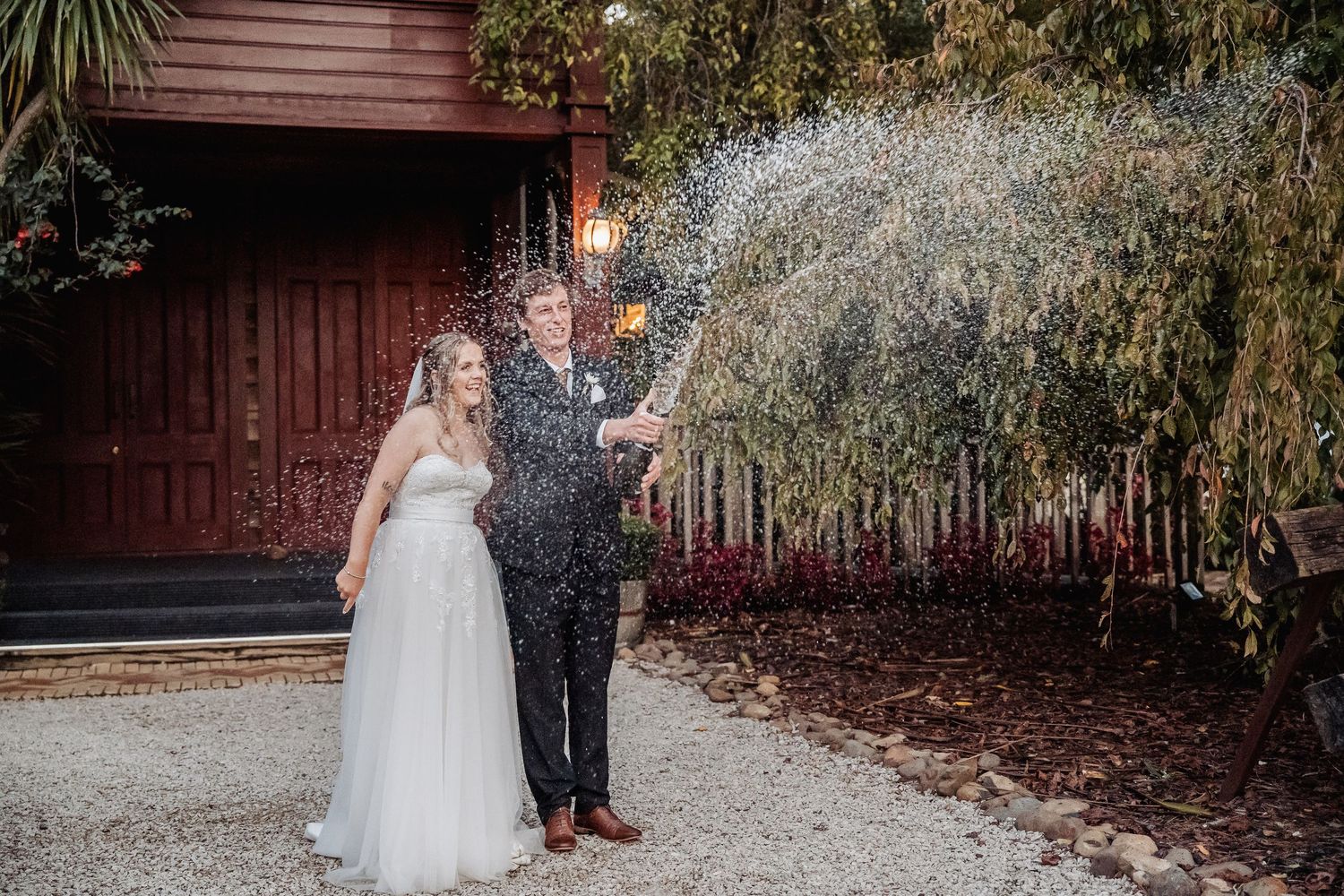A couple celebrates their wedding day with sparklers outside a rustic red building.